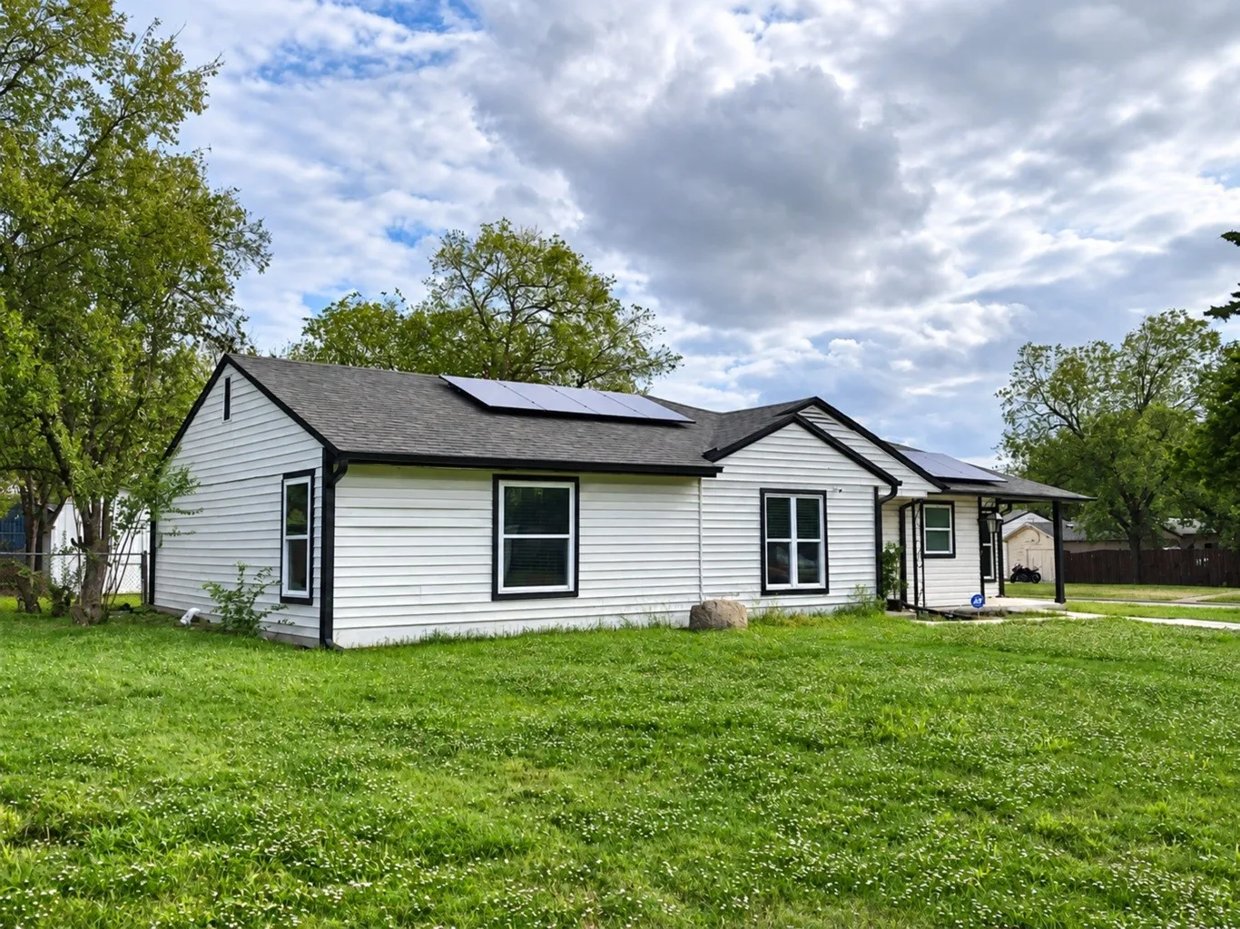 Single-story residence featuring white horizontal siding, a dark shingle roof, roof-mounted solar panels, and a covered front porch entrance