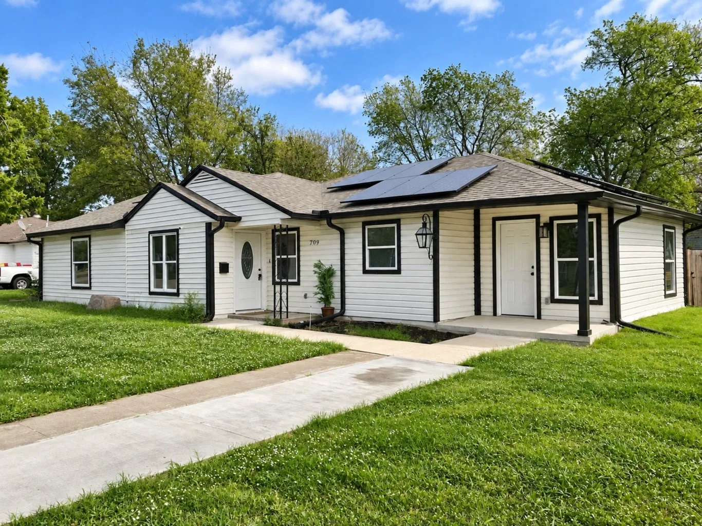 Exterior featuring white horizontal siding, black window trim, roof-mounted solar panels, and a covered concrete entry porch