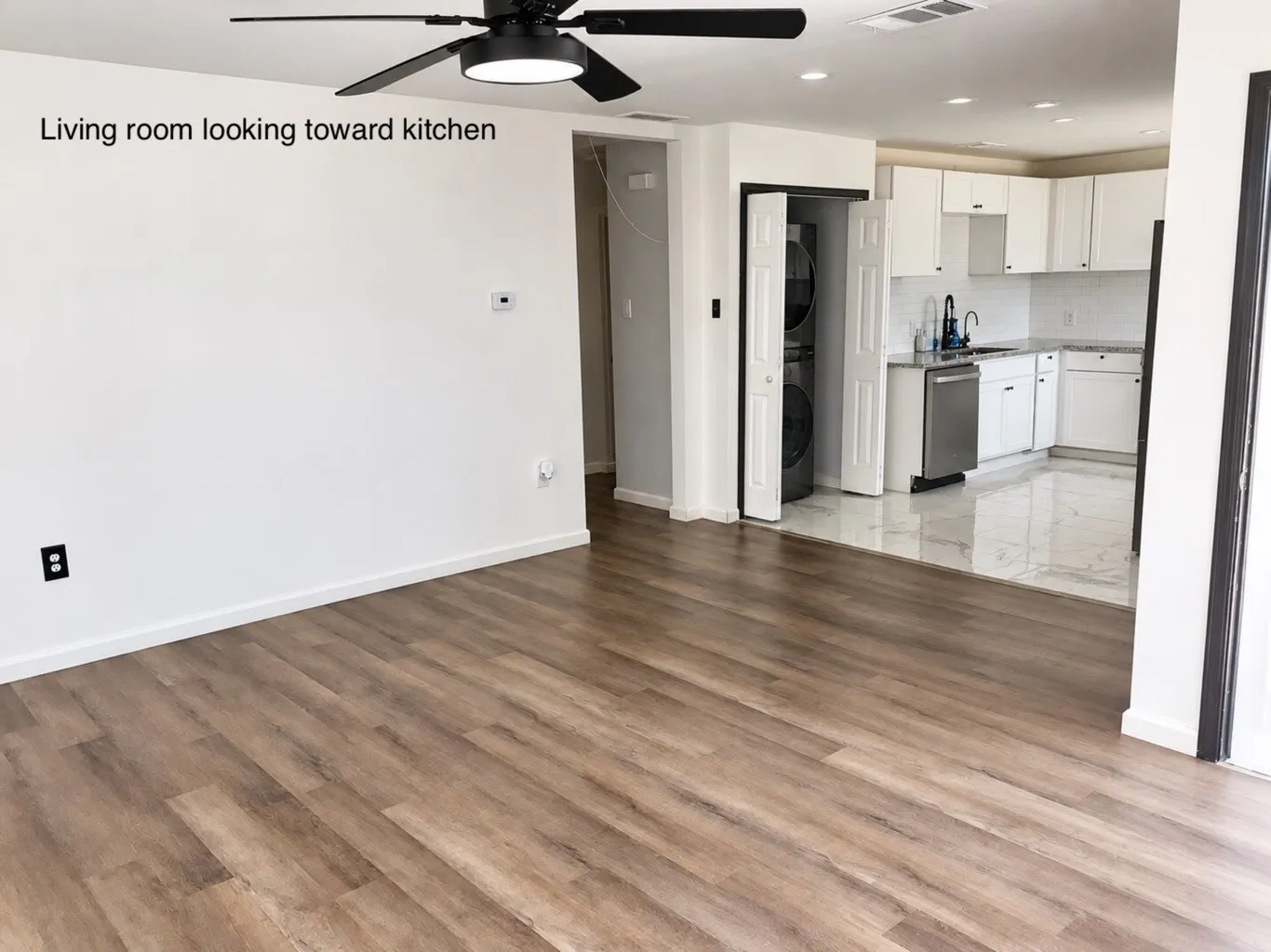 Wood-finish flooring, matte black ceiling fan with integrated lighting, recessed ceiling lights, white cabinetry, and polished stone-finish floor tiling