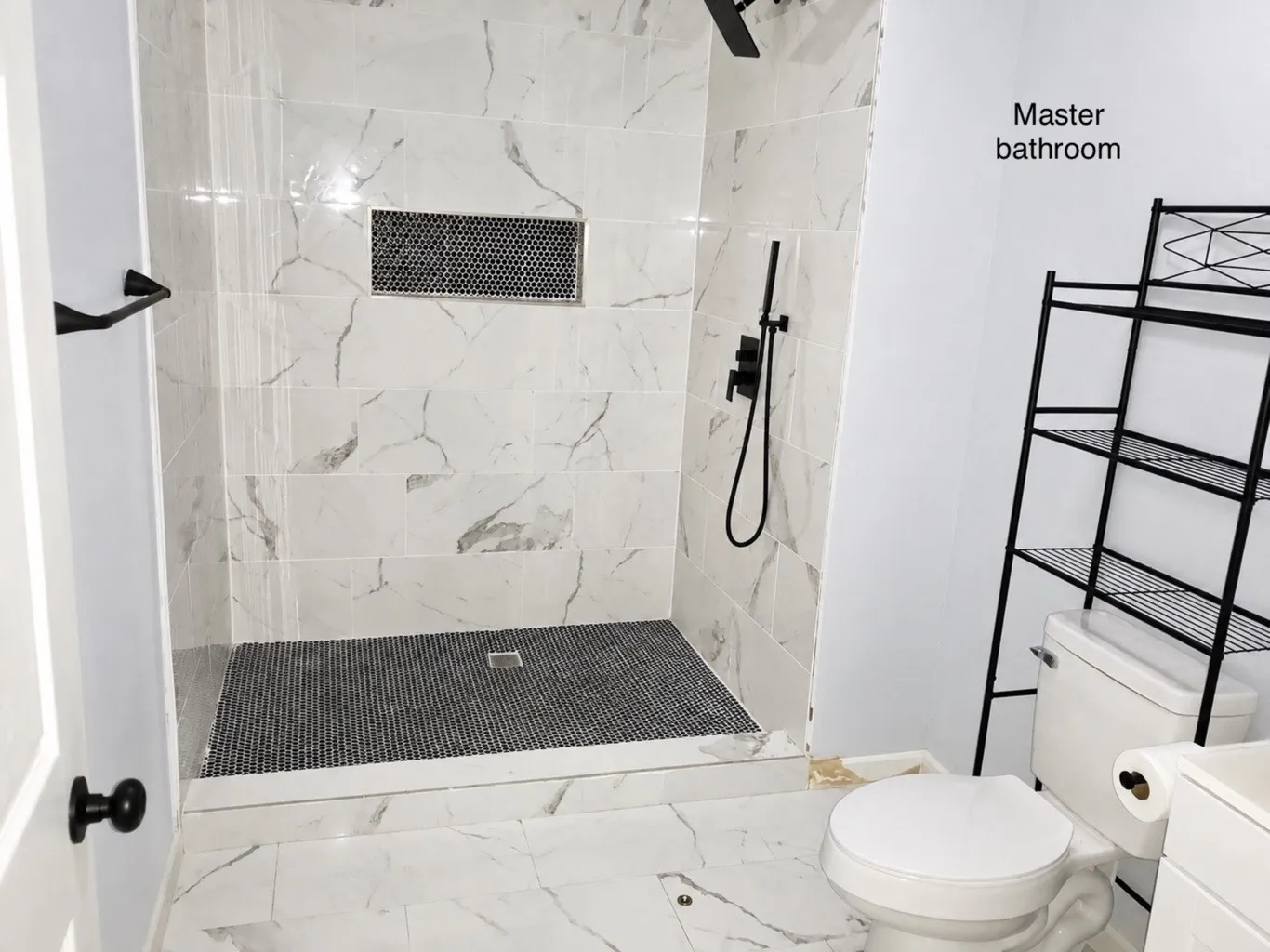 Walk-in shower featuring large-format stone-patterned wall tile, a mosaic-tiled floor, a built-in recessed wall niche, and matte black plumbing fixtures