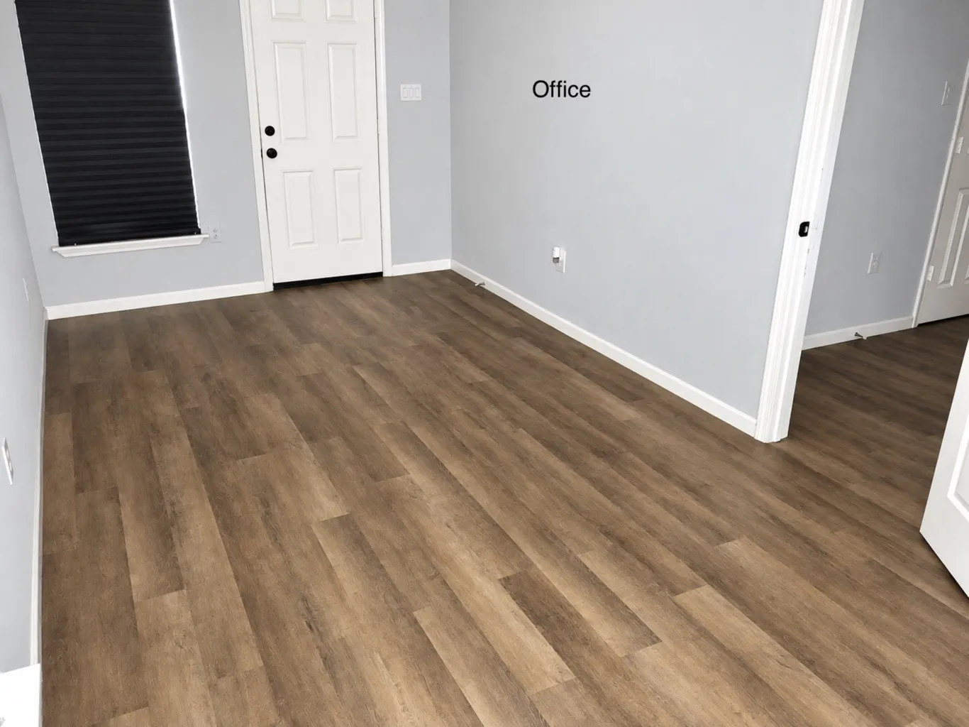 Room featuring wood-finish flooring, neutral wall paint, a multi-panel door, and a single-hung window with a dark window shade