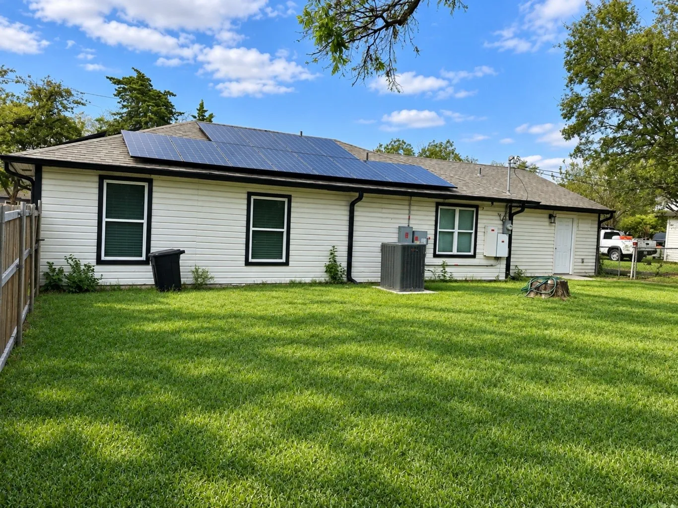 Exterior featuring white siding, roof-mounted solar panels, an asphalt shingle roof, and a fenced backyard