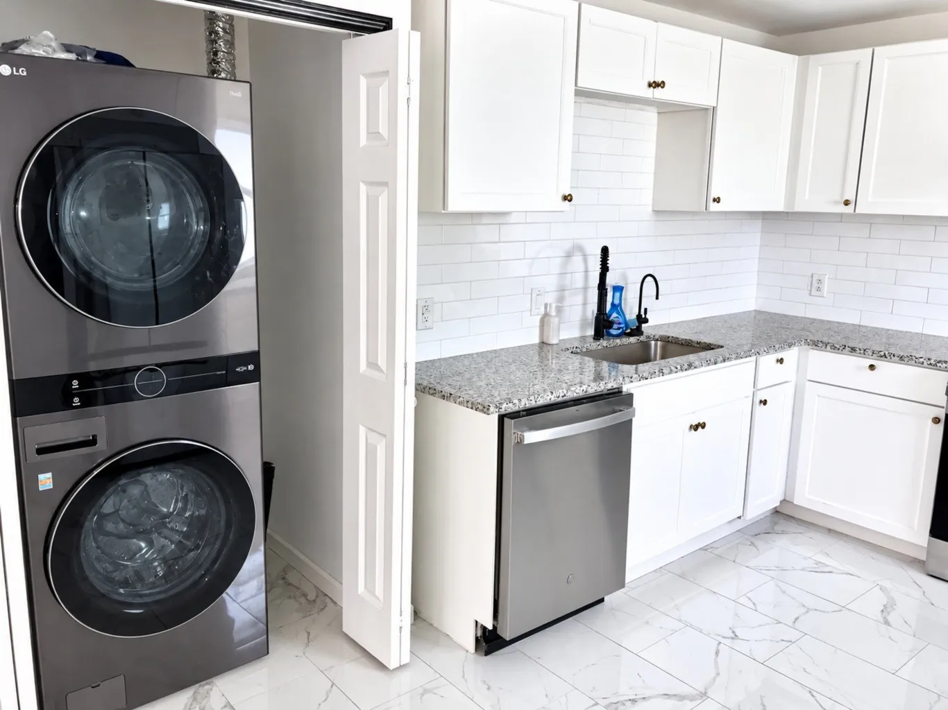 Kitchen featuring shaker-style white cabinetry, stone-finish countertops, subway tile backsplash, stainless steel dishwasher, and large-format tile flooring with marble-finish veining