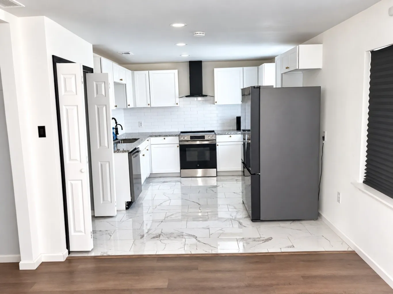 Kitchen featuring white Shaker-style cabinetry, stone-finish countertops, white subway tile backsplash, stainless steel appliances, and large-format rectified tile flooring