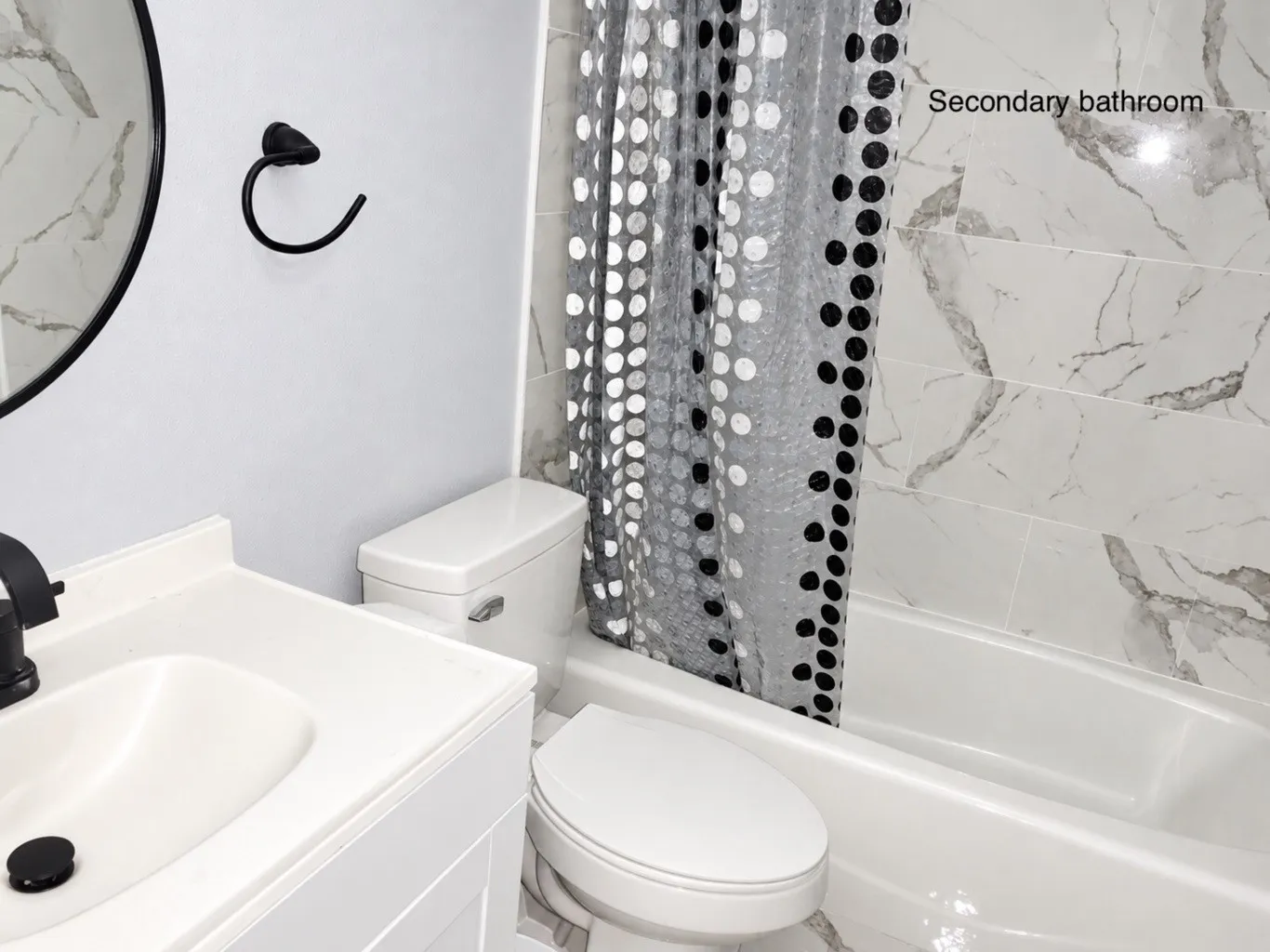 Bathroom featuring a white vanity with integrated sink, matte black faucet, wall-mounted circular mirror, and tile surround bathtub