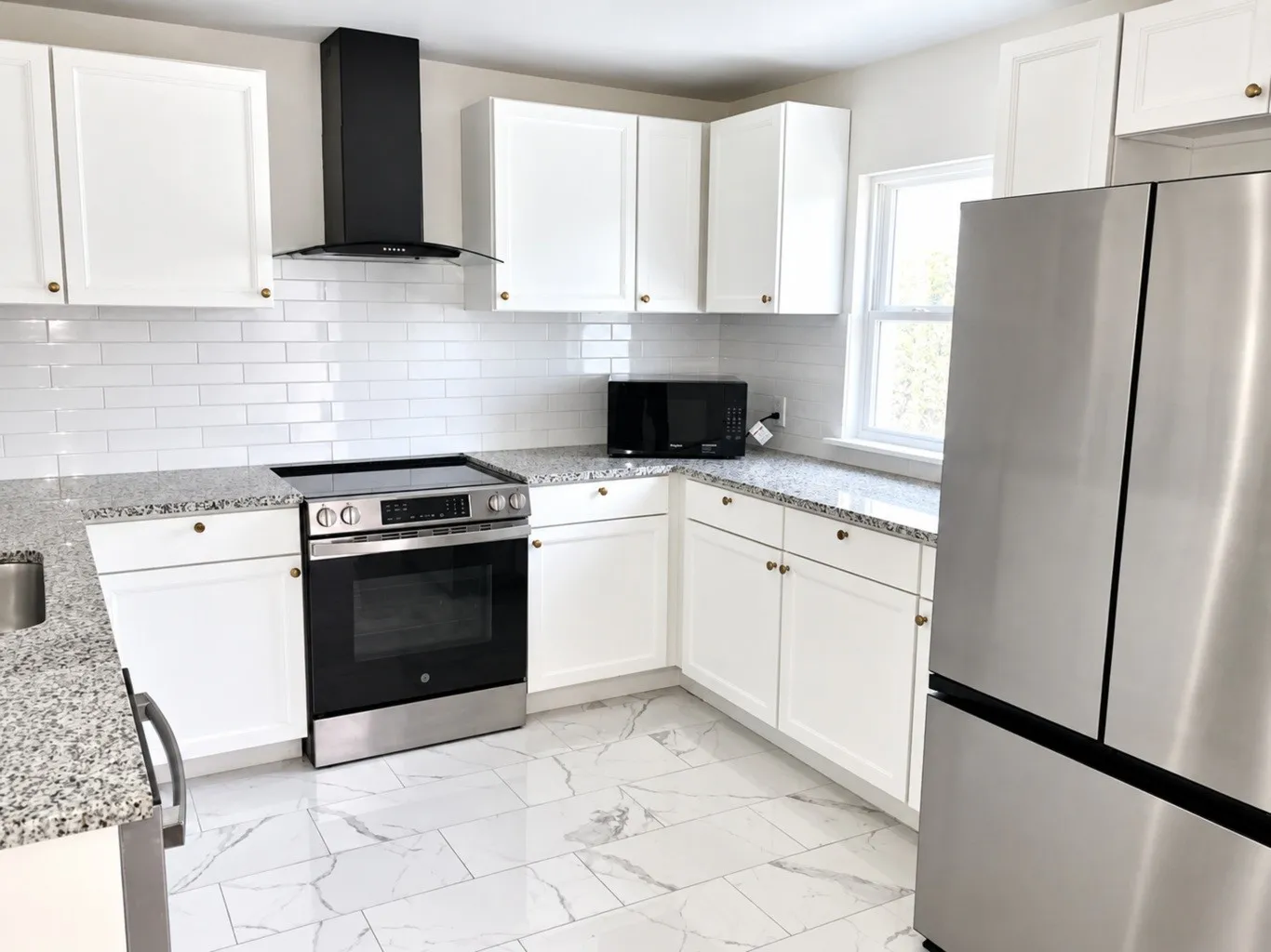 Kitchen featuring white shaker-style cabinetry, speckled stone countertops, white subway tile backsplash, stainless steel appliances, and large-format porcelain tile flooring