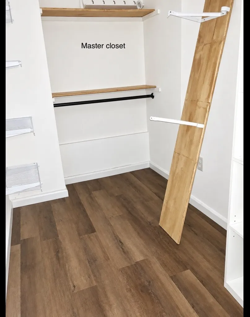 Walk-in storage space featuring wood-finish flooring, built-in open shelving, and a mounted metal garment rod