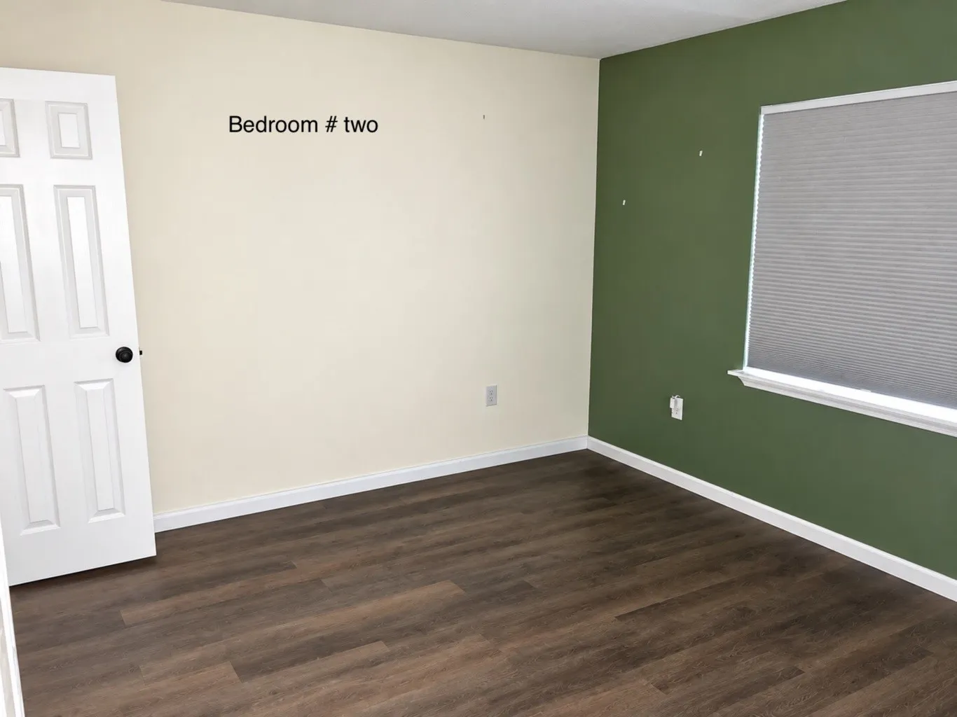 Room featuring wood-finish flooring, a six-panel door, and a cellular shade window treatment
