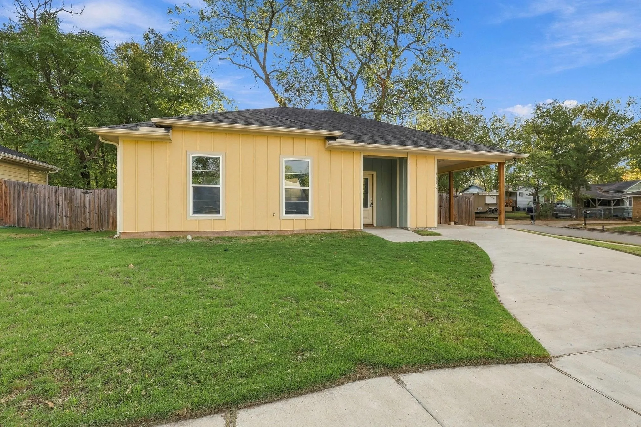 Single-story exterior featuring vertical board-and-batten siding, a covered carport, a concrete driveway, and a fenced yard
