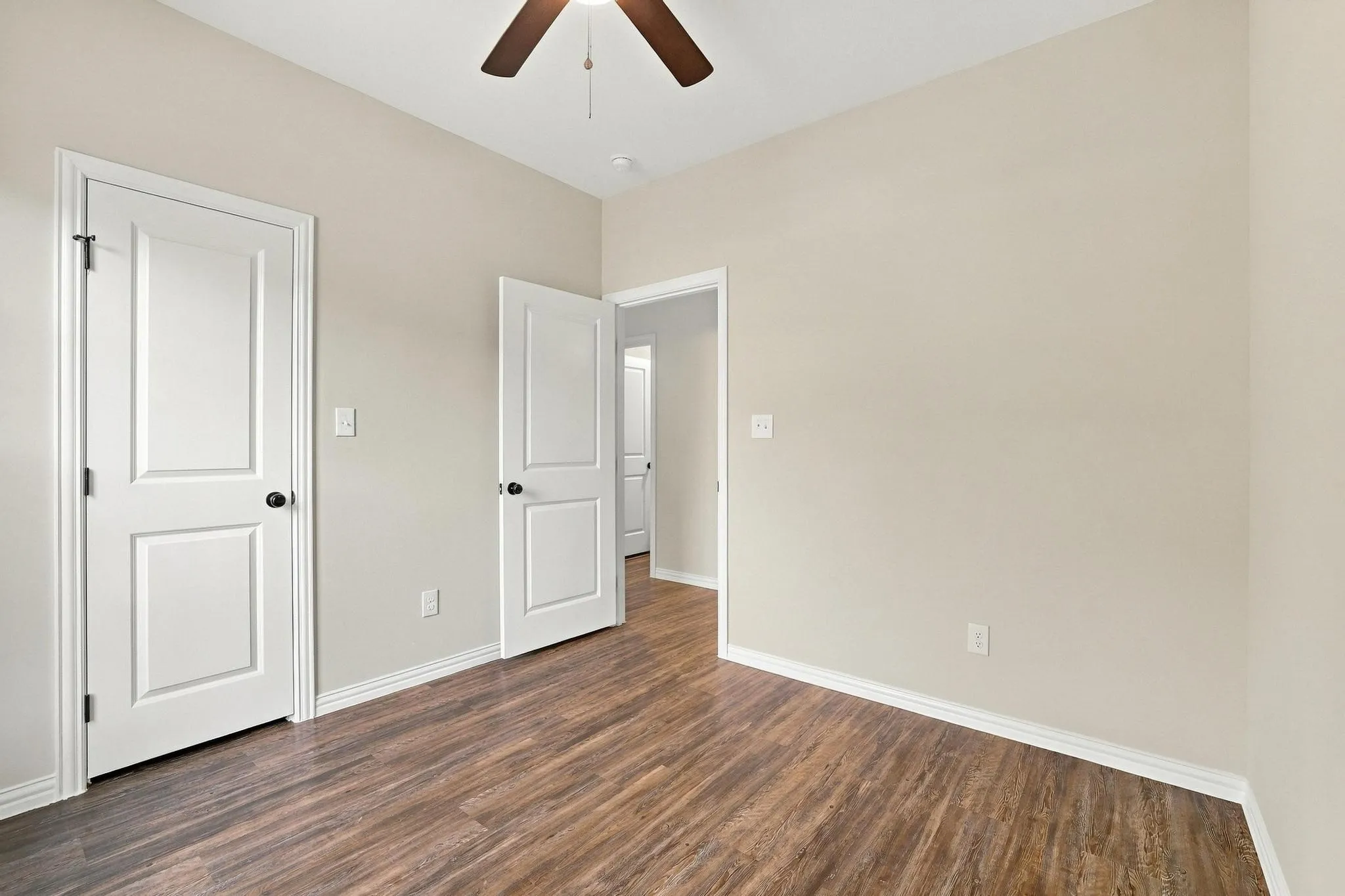 Room featuring wood-finish flooring, two-panel interior doors, and a ceiling-mounted paddle fan