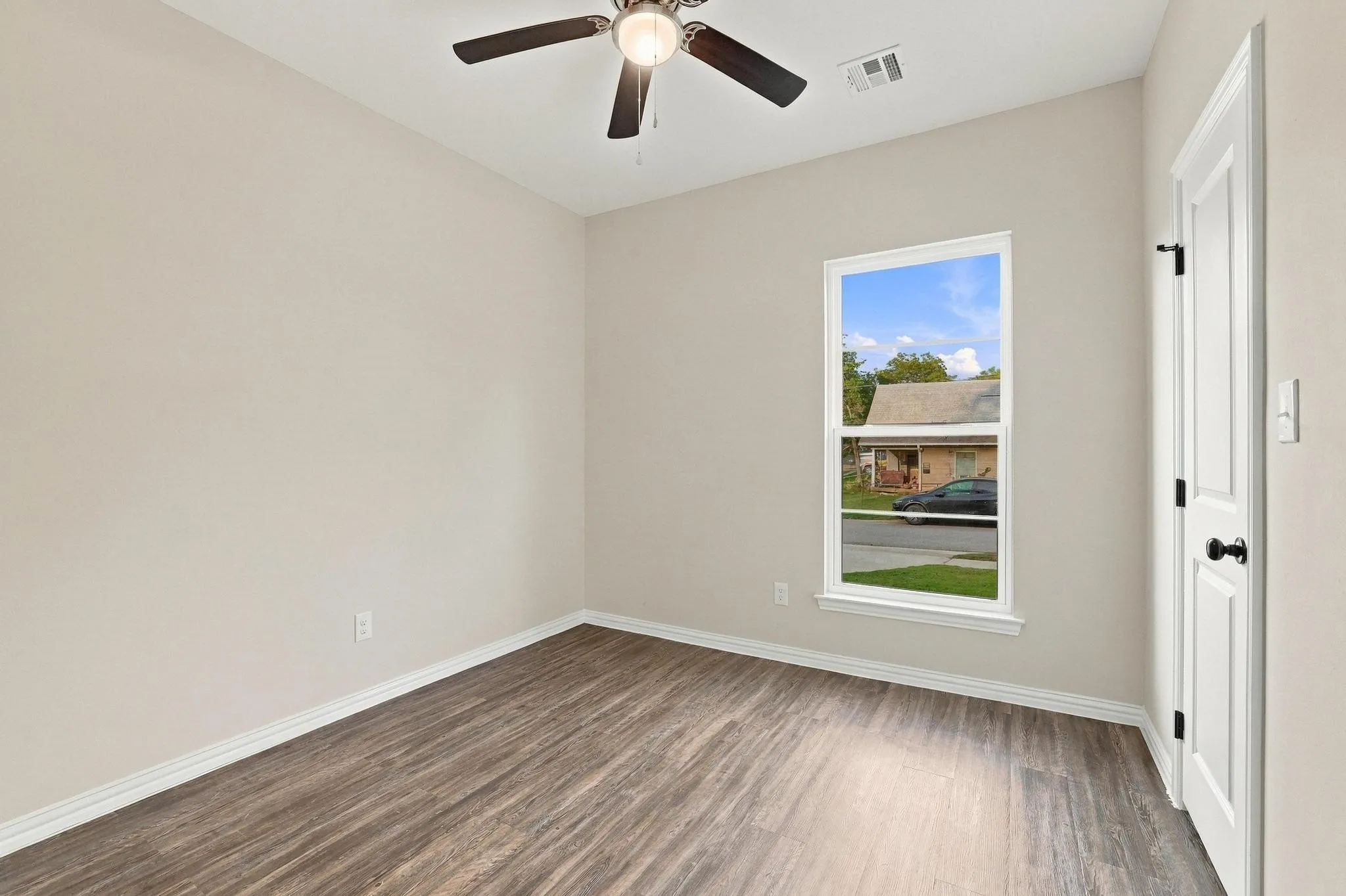 Neutral-toned interior room featuring wood-finish flooring, a ceiling fan with integrated lighting, and a single-hung window