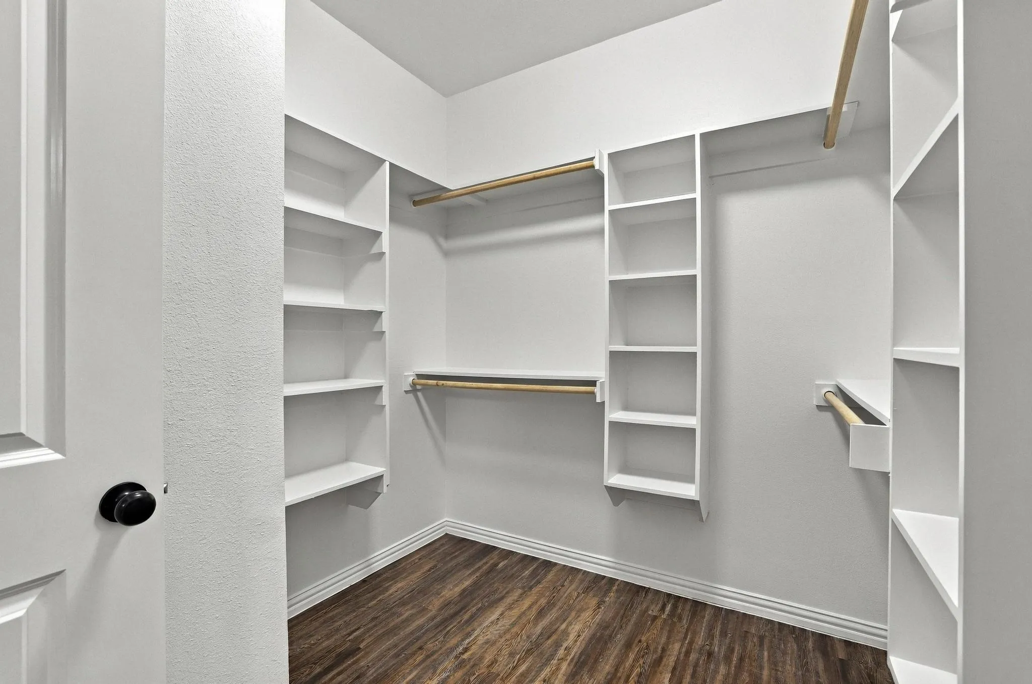 Walk-in closet featuring white built-in shelving, wooden garment rods, and dark wood-finish flooring