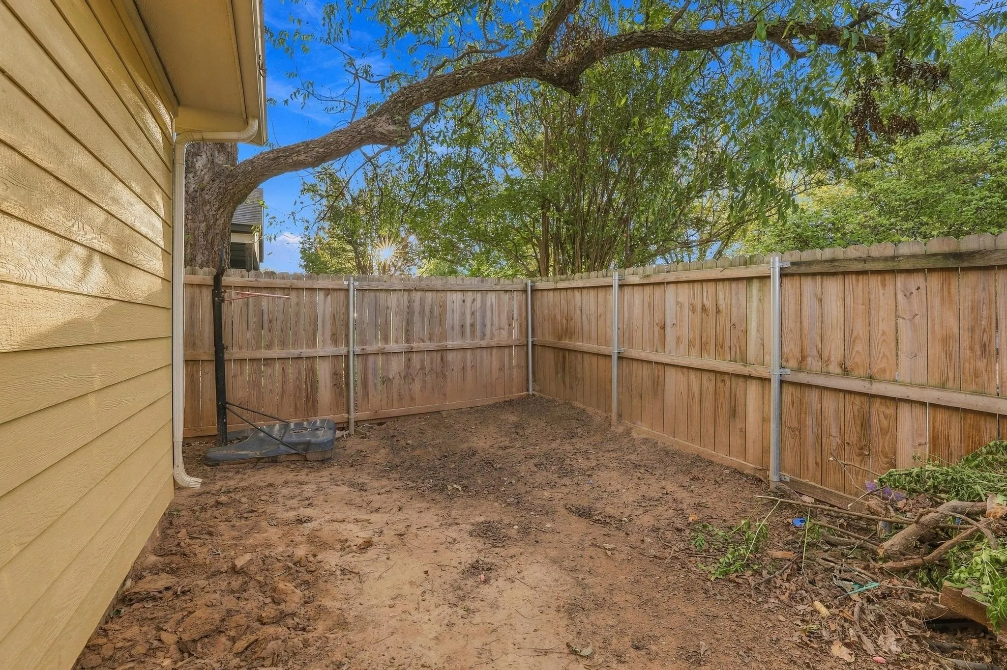 Exterior side yard featuring horizontal lap siding, a wood-panel privacy fence, and mature trees