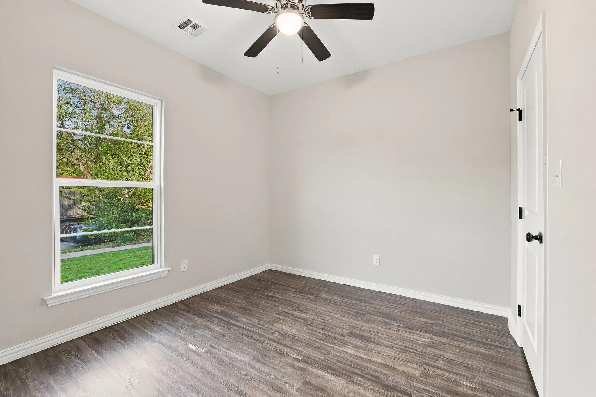 Interior space featuring wood-finish flooring, a single-hung window with muntins, a ceiling fan with integrated lighting, and a solid-core door with matte black hardware