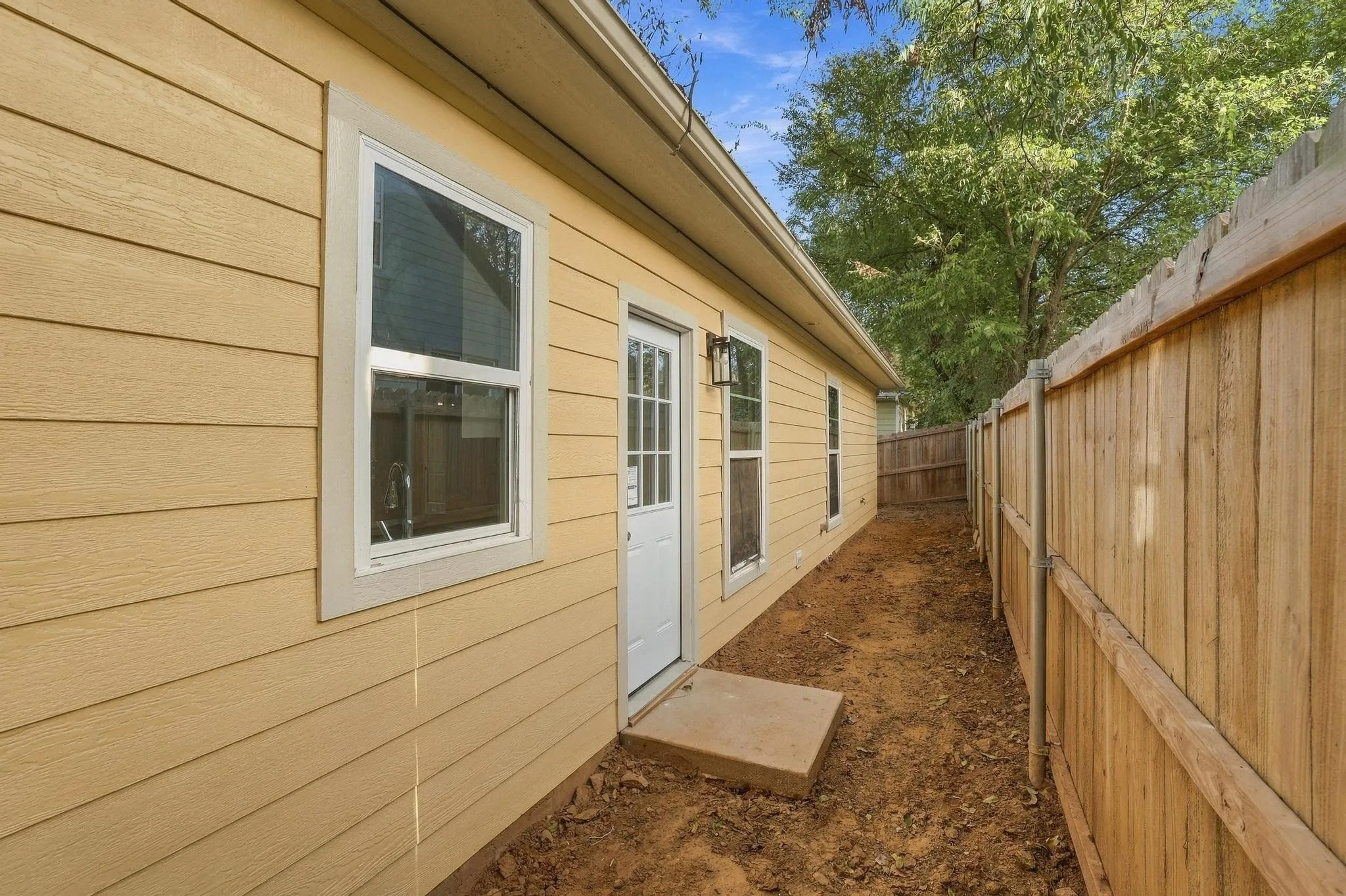 Horizontal lap siding exterior with a white-framed single entry door, concrete threshold, and wood privacy fencing