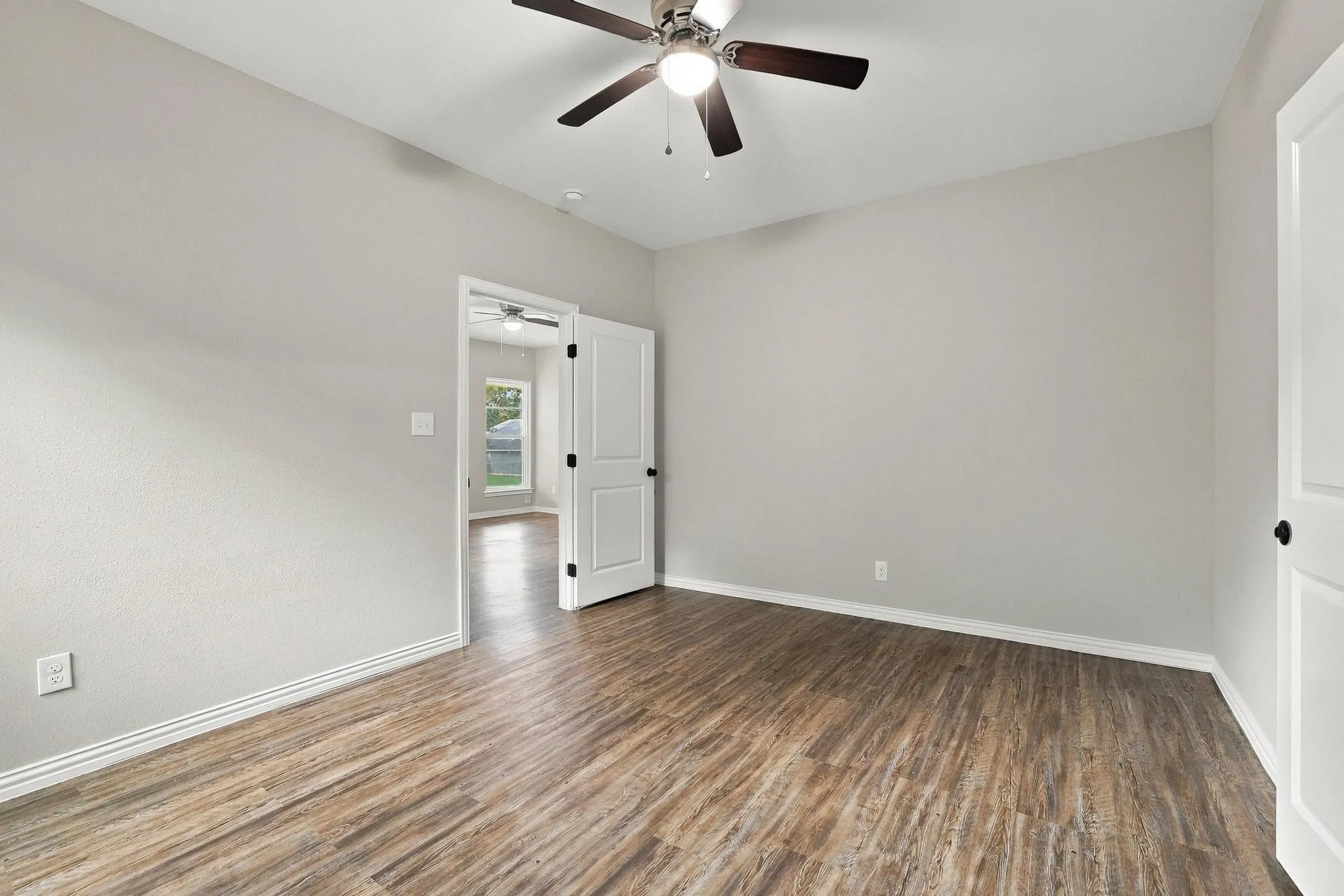 Neutral interior featuring wood-finish flooring, a ceiling fan with integrated lighting, and multi-panel doors
