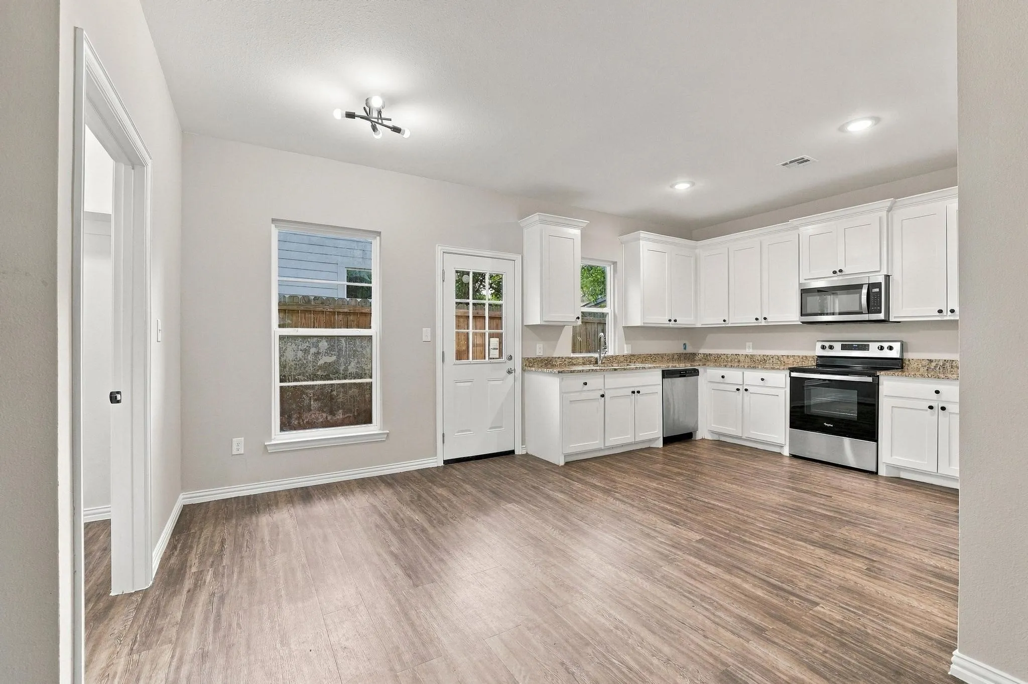 Kitchen featuring white shaker-style cabinetry, stone-finish countertops, stainless steel appliances, and wood-finish flooring