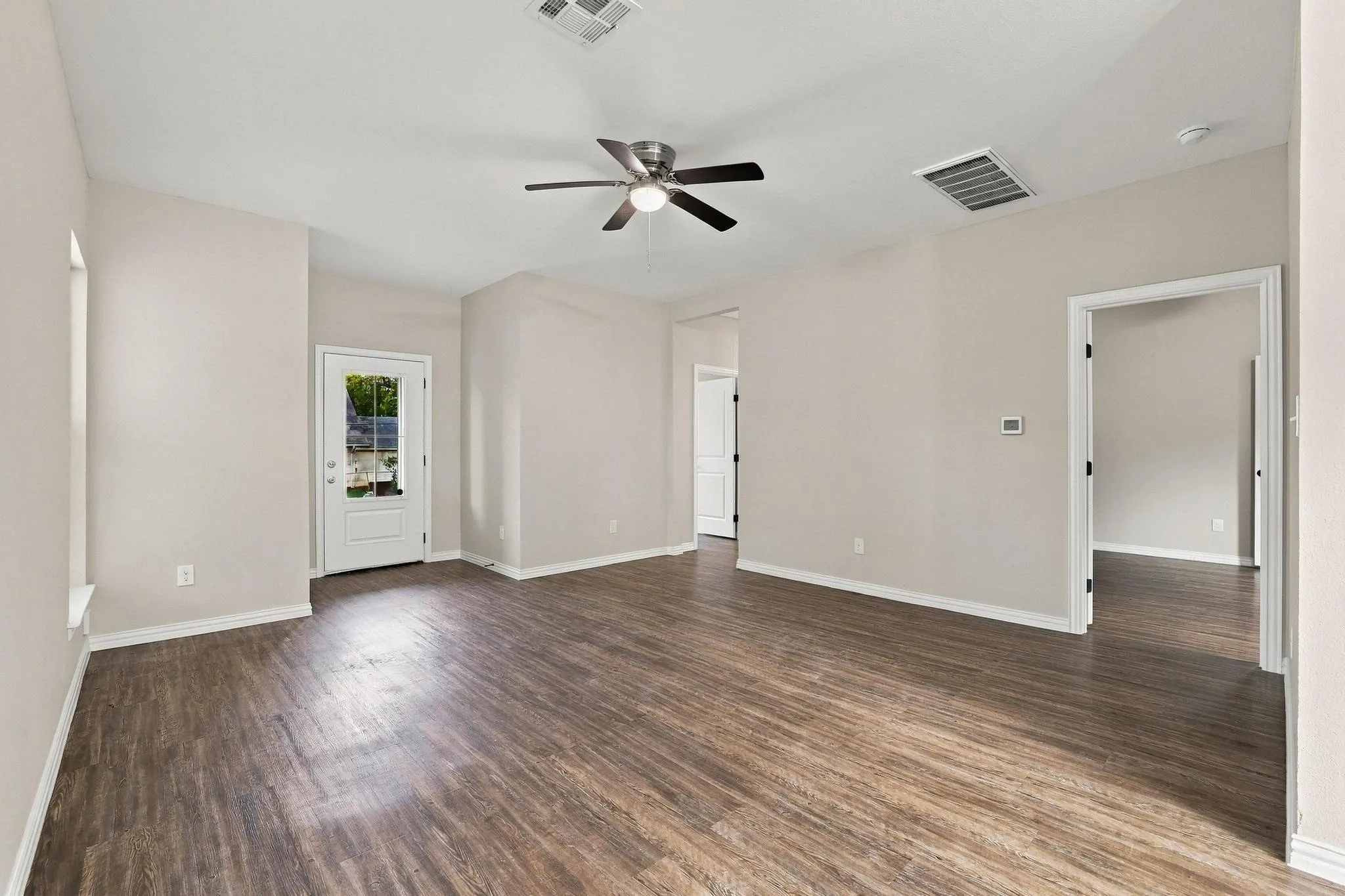 Open-concept area featuring wood-finish flooring, neutral wall paint, vaulted ceilings, and a ceiling fan with integrated lighting