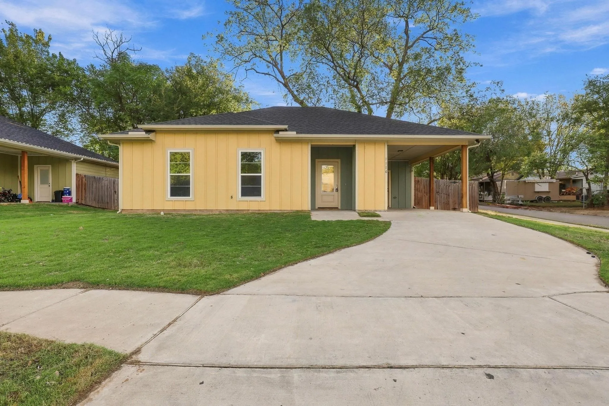 Single-story residence featuring vertical siding, a covered carport with wood-finish supports, a concrete driveway, and an expansive front lawn