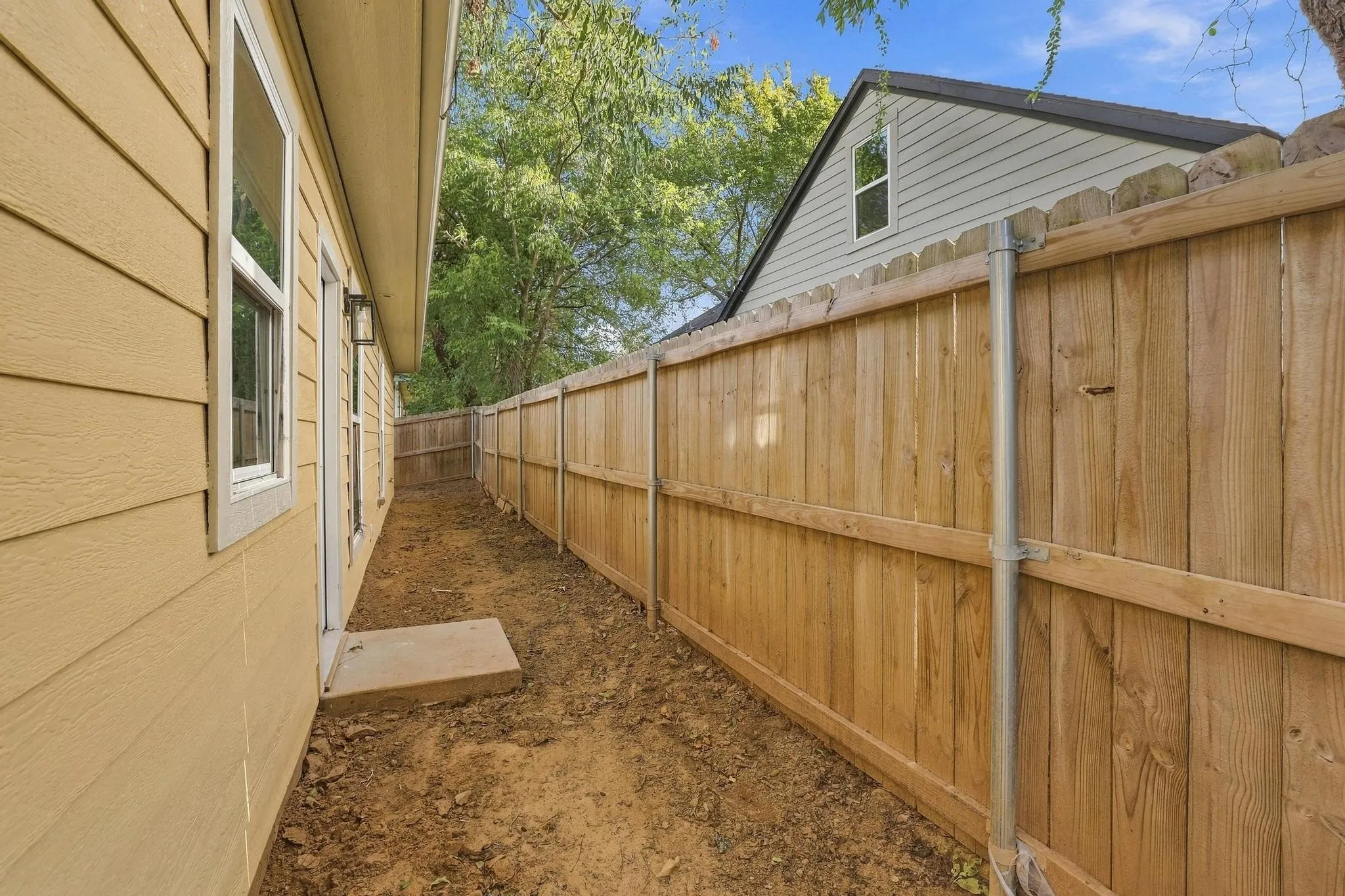 Side yard featuring horizontal lap siding, a concrete landing, and a wood privacy fence with metal support posts