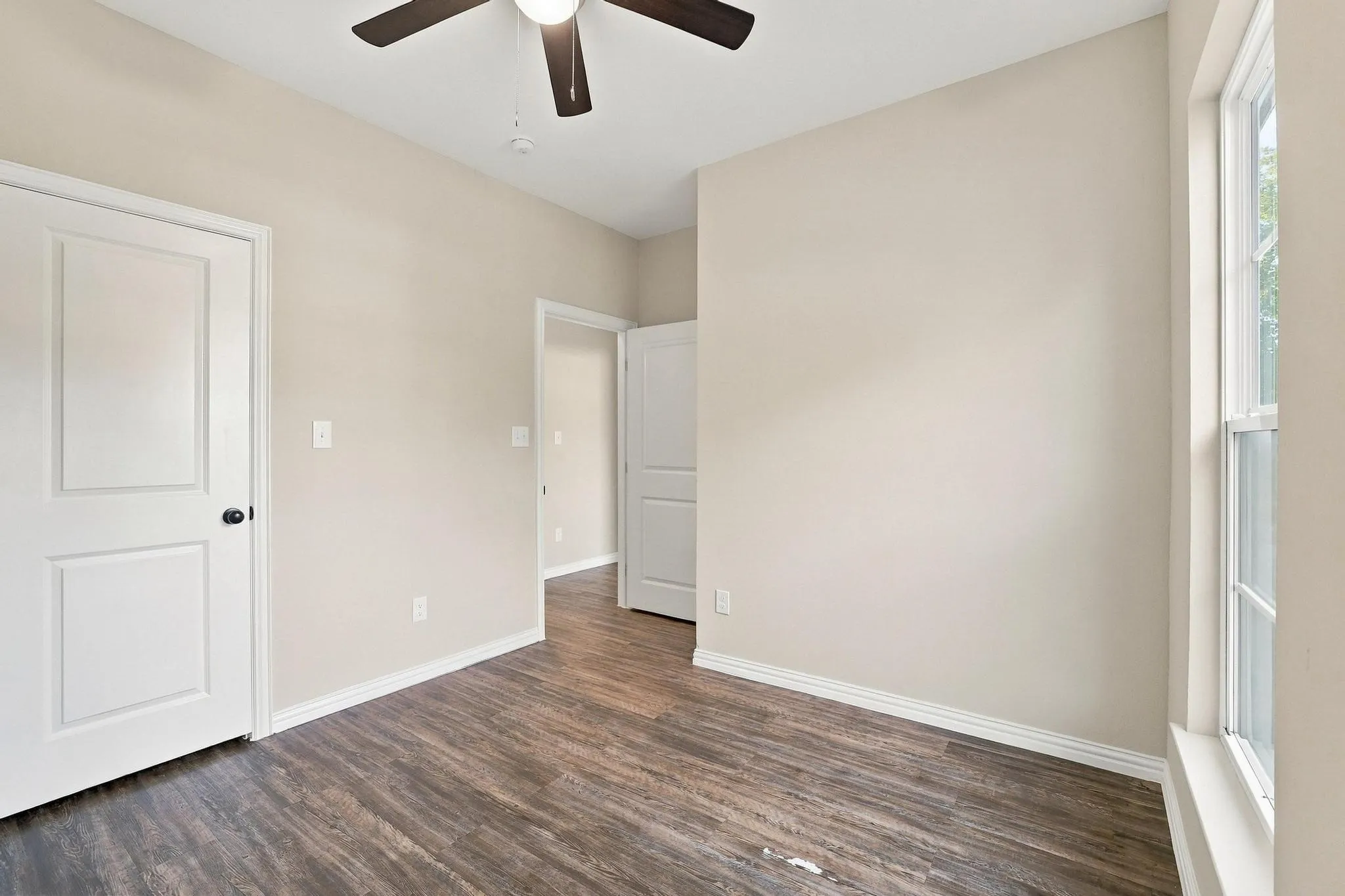 Interior space featuring wood-finish flooring, neutral wall paint, multi-panel interior doors, and a ceiling-mounted light fixture with a fan