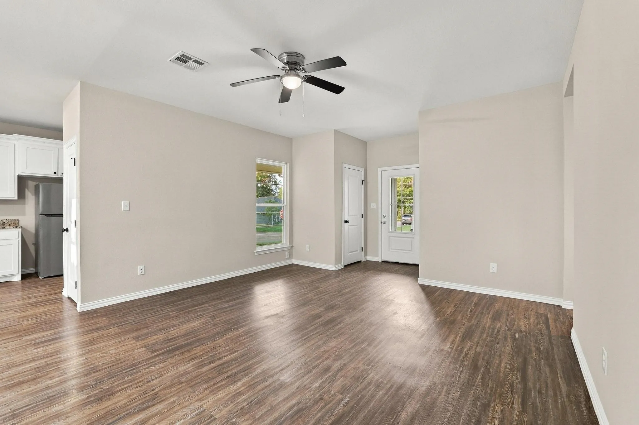 Open interior space featuring wood-finish flooring, neutral wall paint, a central ceiling fan with integrated lighting, and a glass-paneled exterior door
