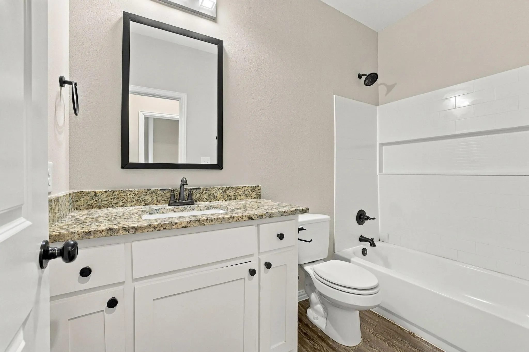 Bathroom featuring white shaker-style cabinetry, stone-finish countertop, undermount sink, matte black hardware, and a tub-shower combination with white subway-style wall tiling