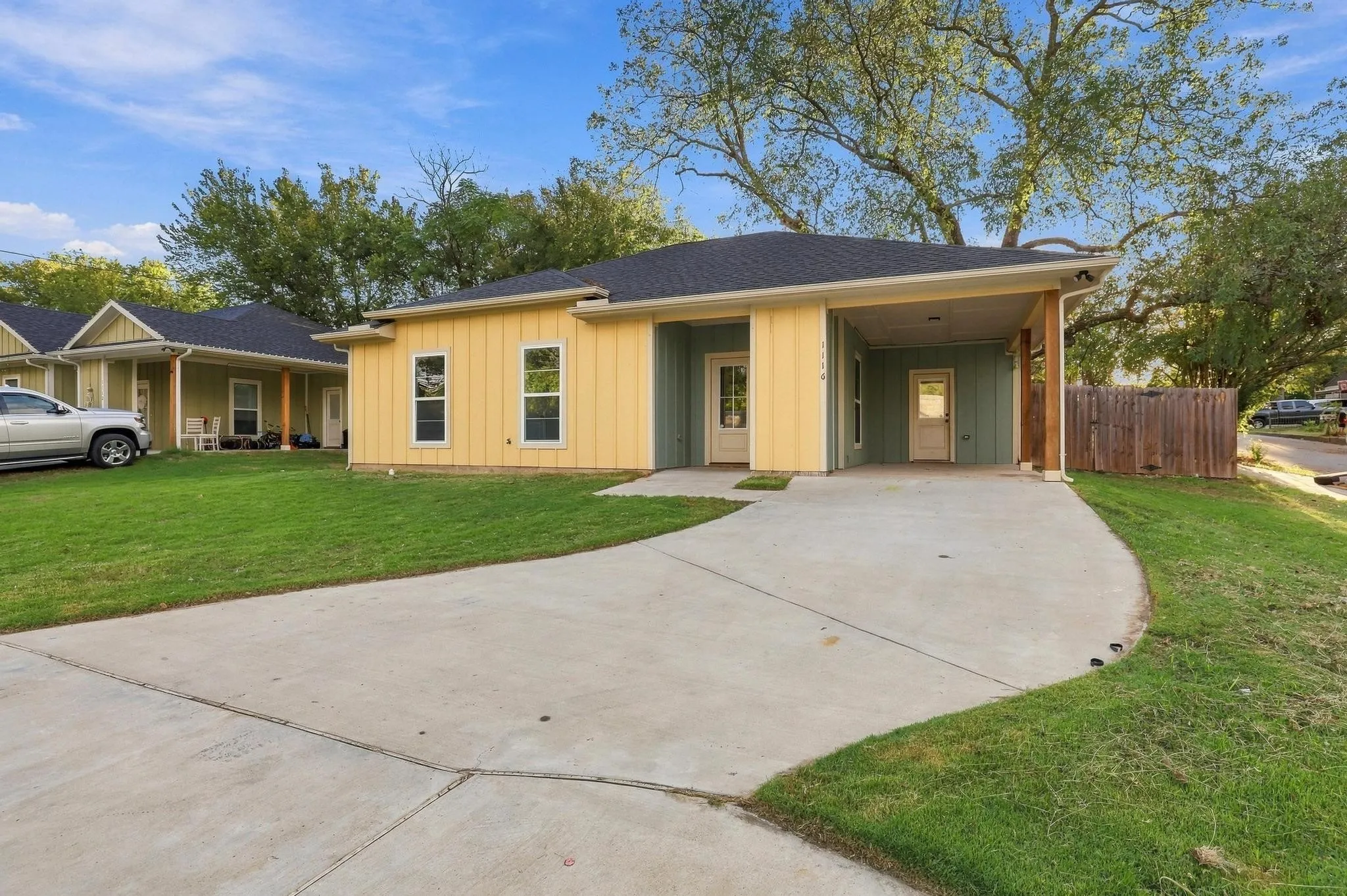 Single-story exterior featuring vertical board-and-batten siding, a covered entryway, a concrete driveway, an attached carport, and a wood privacy fence