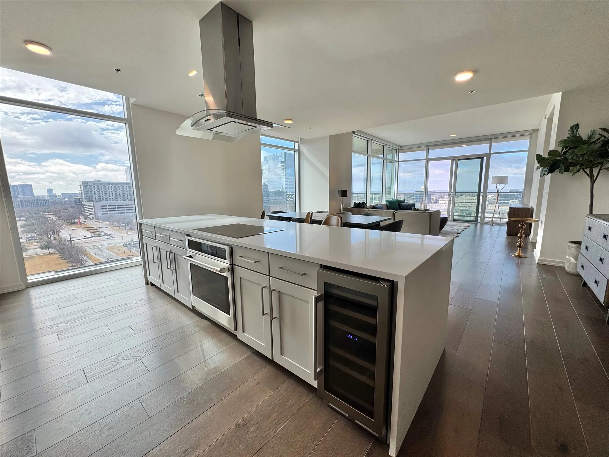Kitchen with island range hood, white cabinetry, oven, beverage cooler, and a wall of windows