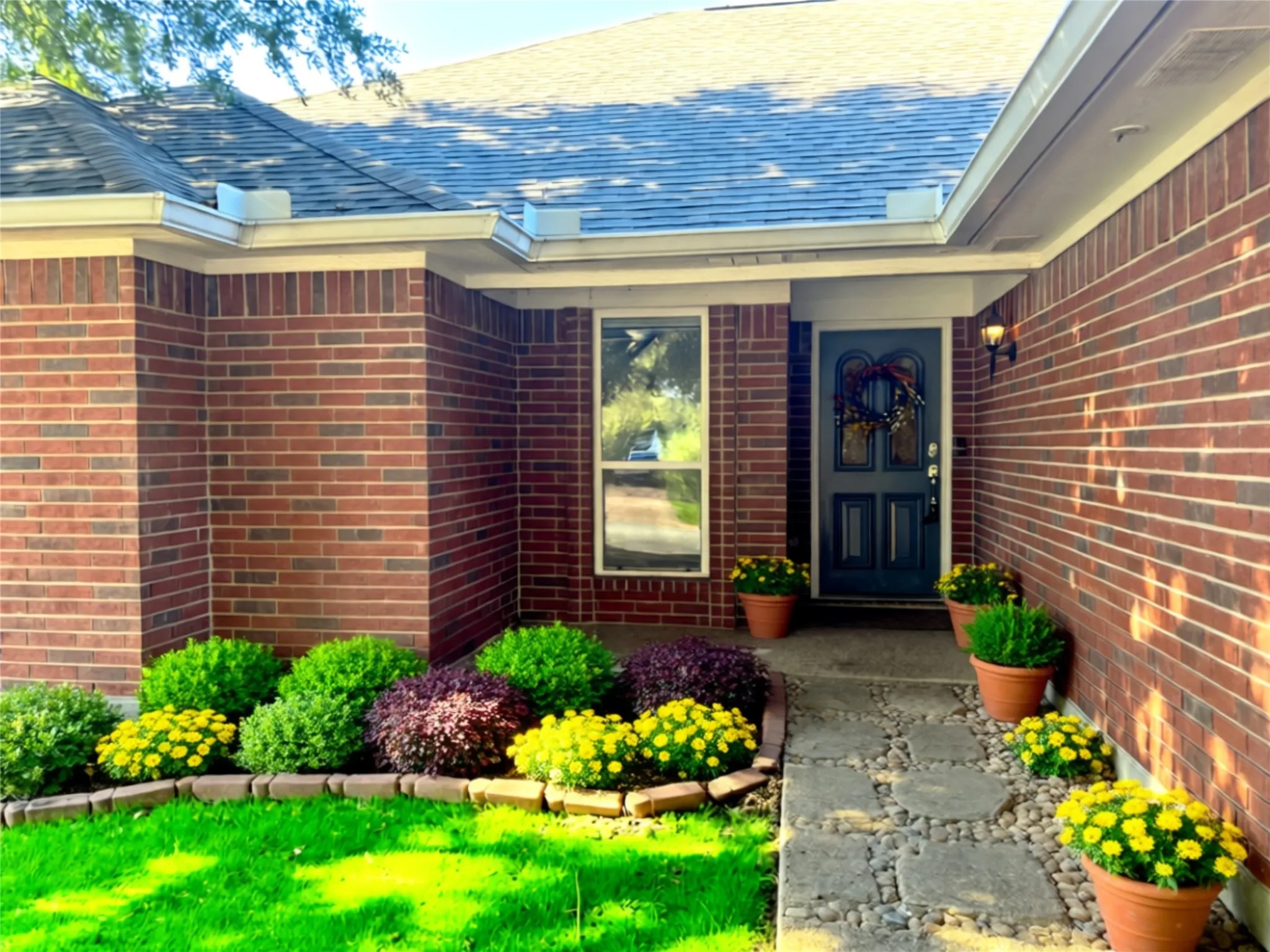 Brick exterior featuring a multi-paned entry door, flagstone walkway, and manicured landscaping