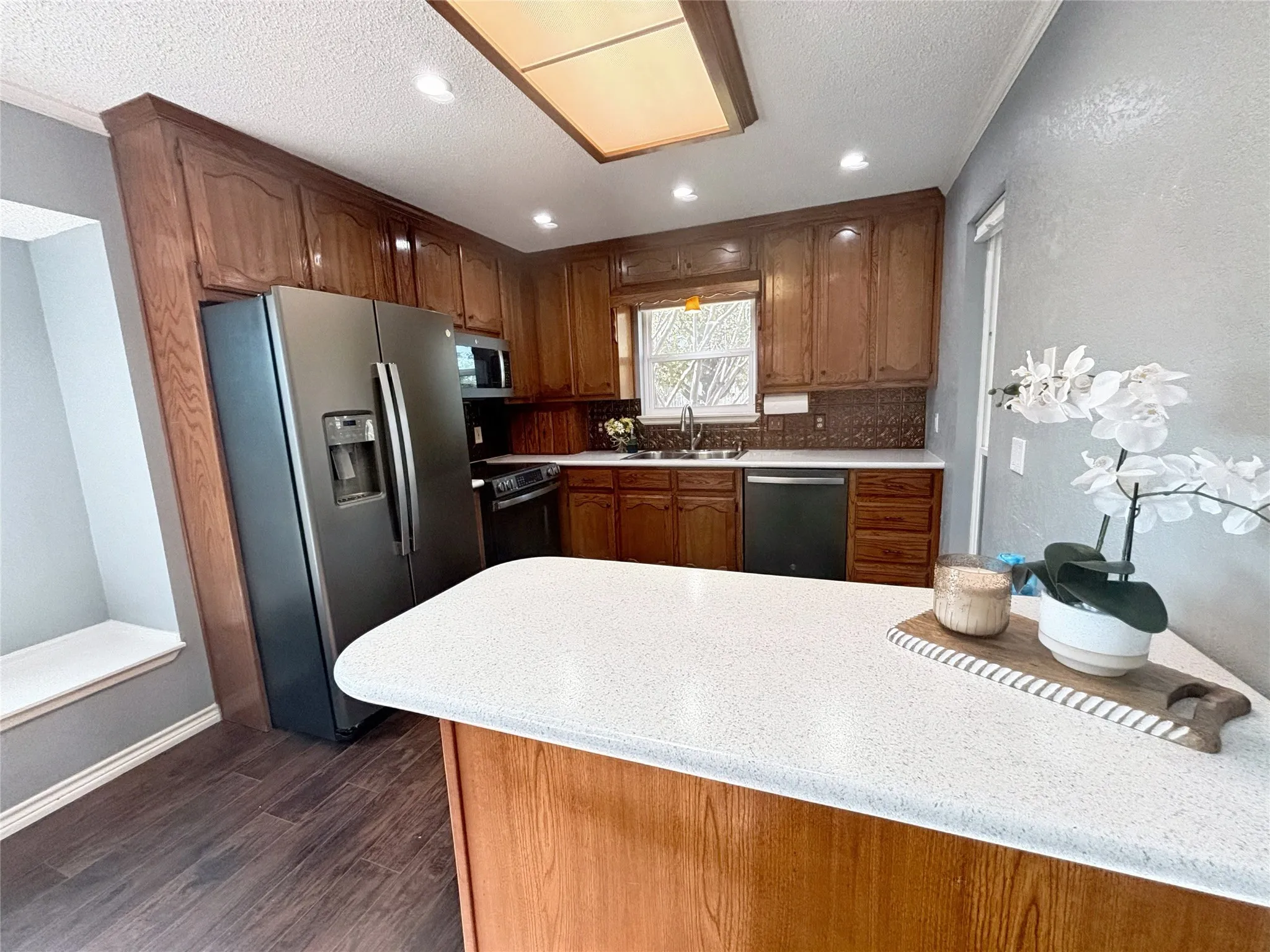 Kitchen featuring wood-finish cabinetry, a white countertop island, stainless steel appliances, a double-basin sink, and wood-finish flooring