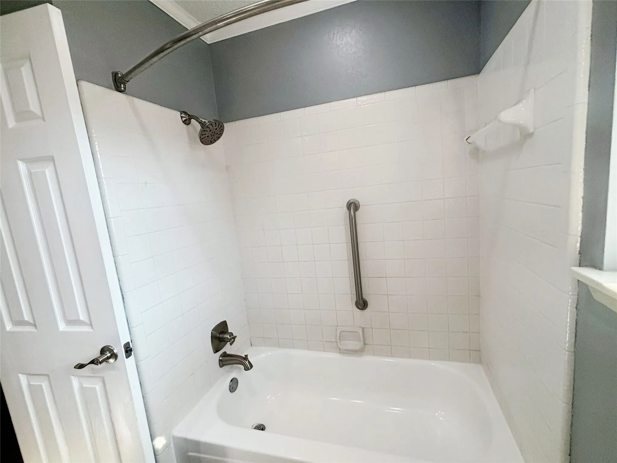 Bathtub with white subway tile surround, polished metal faucet hardware, matching shower head, integrated soap dish, and stainless steel grab bar
