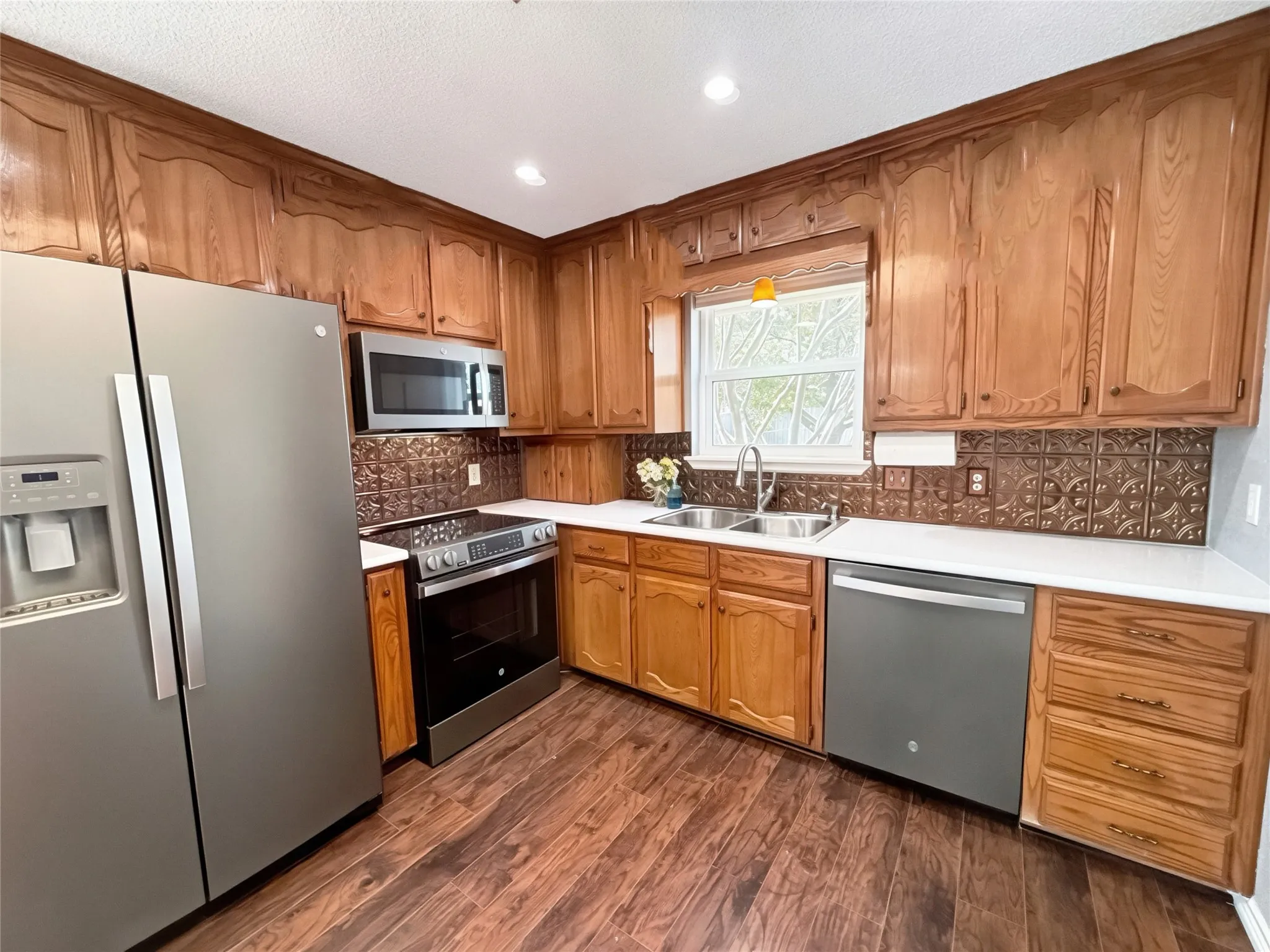 Kitchen featuring stained wood cabinetry, stainless steel appliances, patterned metal tile backsplash, white countertops, and wood-finish flooring