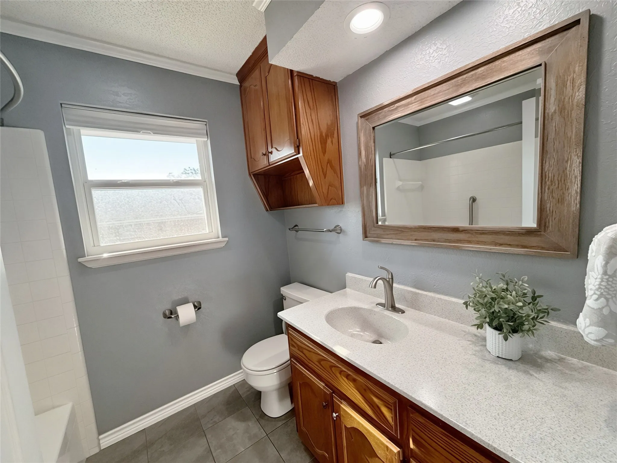Bathroom featuring a vanity with quartz countertop, under-mount sink, integrated wood cabinetry, a framed mirror, and tile flooring