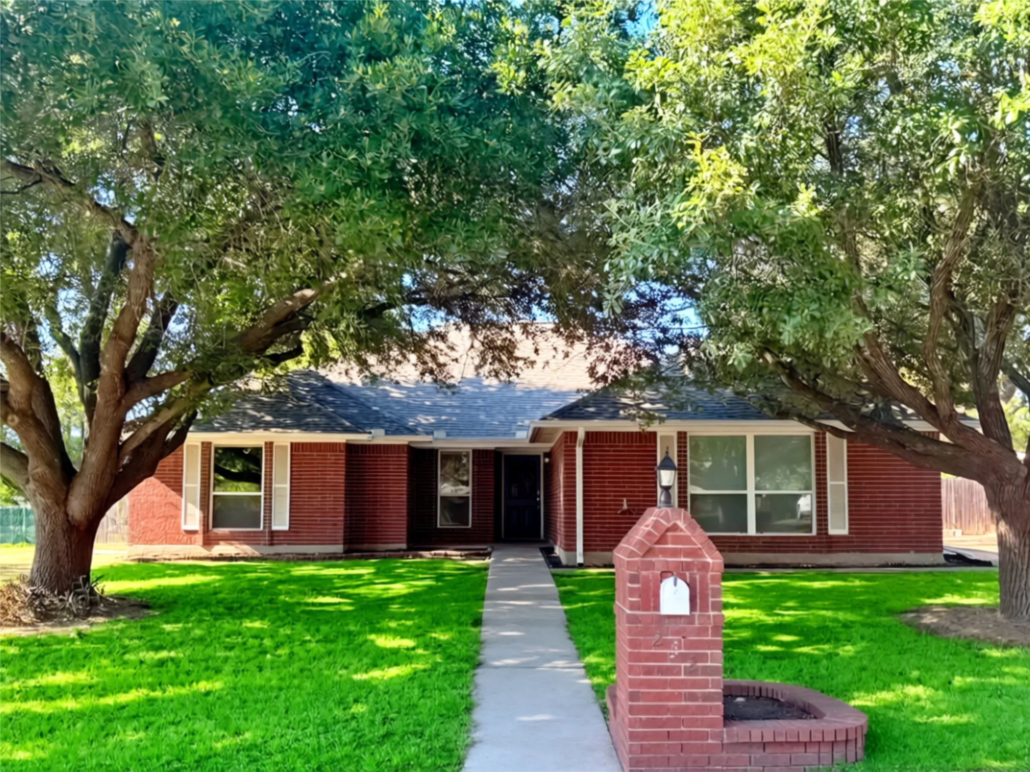 Brick exterior featuring a gabled roof, concrete walkway, matching brick mailbox with integrated planter, and mature shade​​‌​​​​‌​​‌‌​‌‌​​​‌‌​‌​‌​‌​​​‌​​ trees