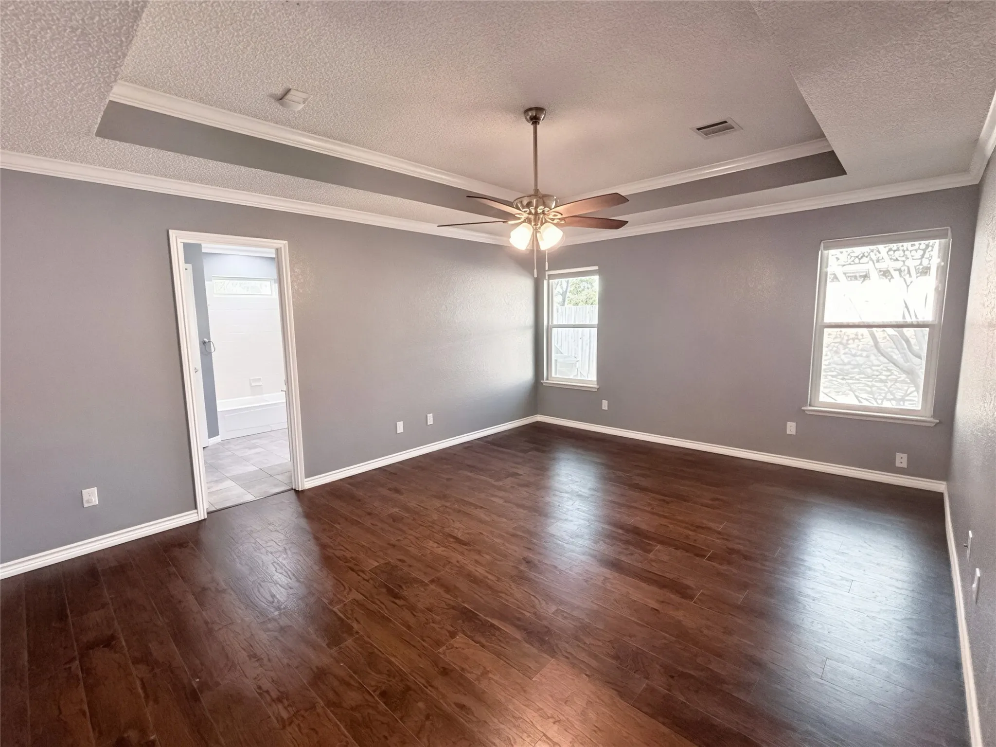 Tray ceiling featuring a central light fixture and ceiling fan, wood-finish flooring, and dual windows
