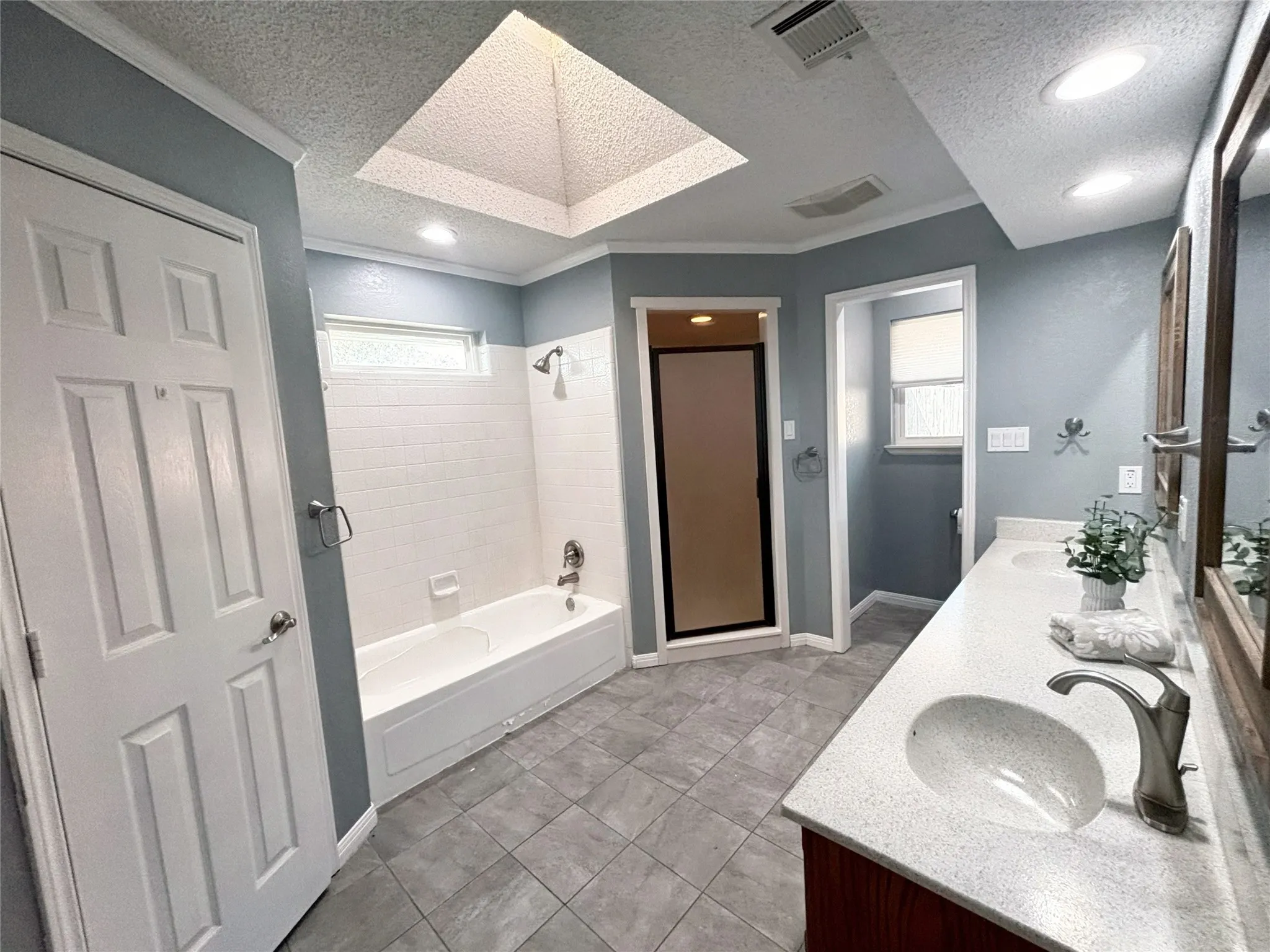 Bathroom featuring a dual-sink vanity with a solid-surface countertop, a skylight, tile flooring, and a separate bathtub and shower enclosure