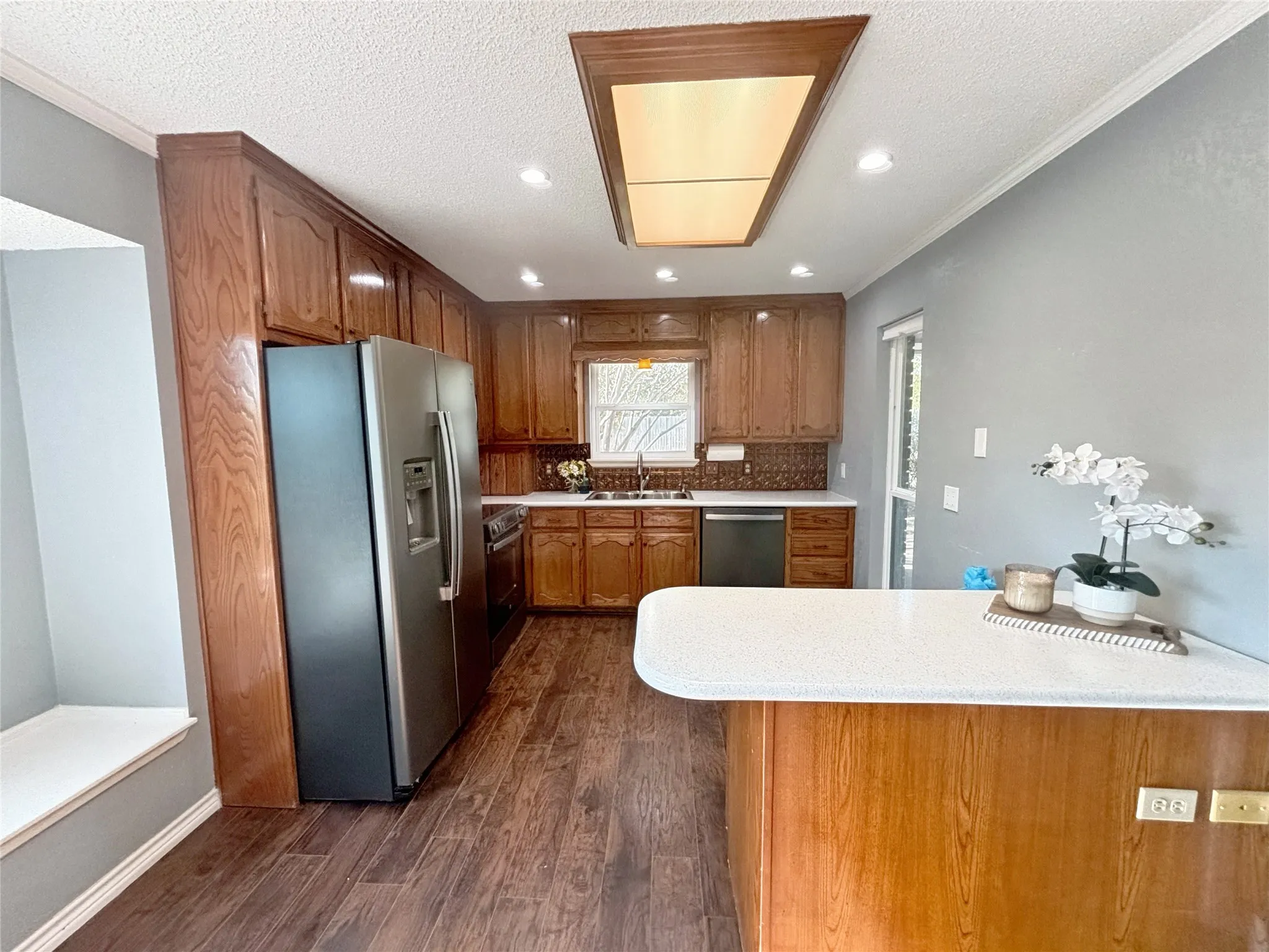 Kitchen featuring wood cabinetry, stainless steel appliances, white solid-surface countertops, wood-finish flooring, and recessed ceiling lighting