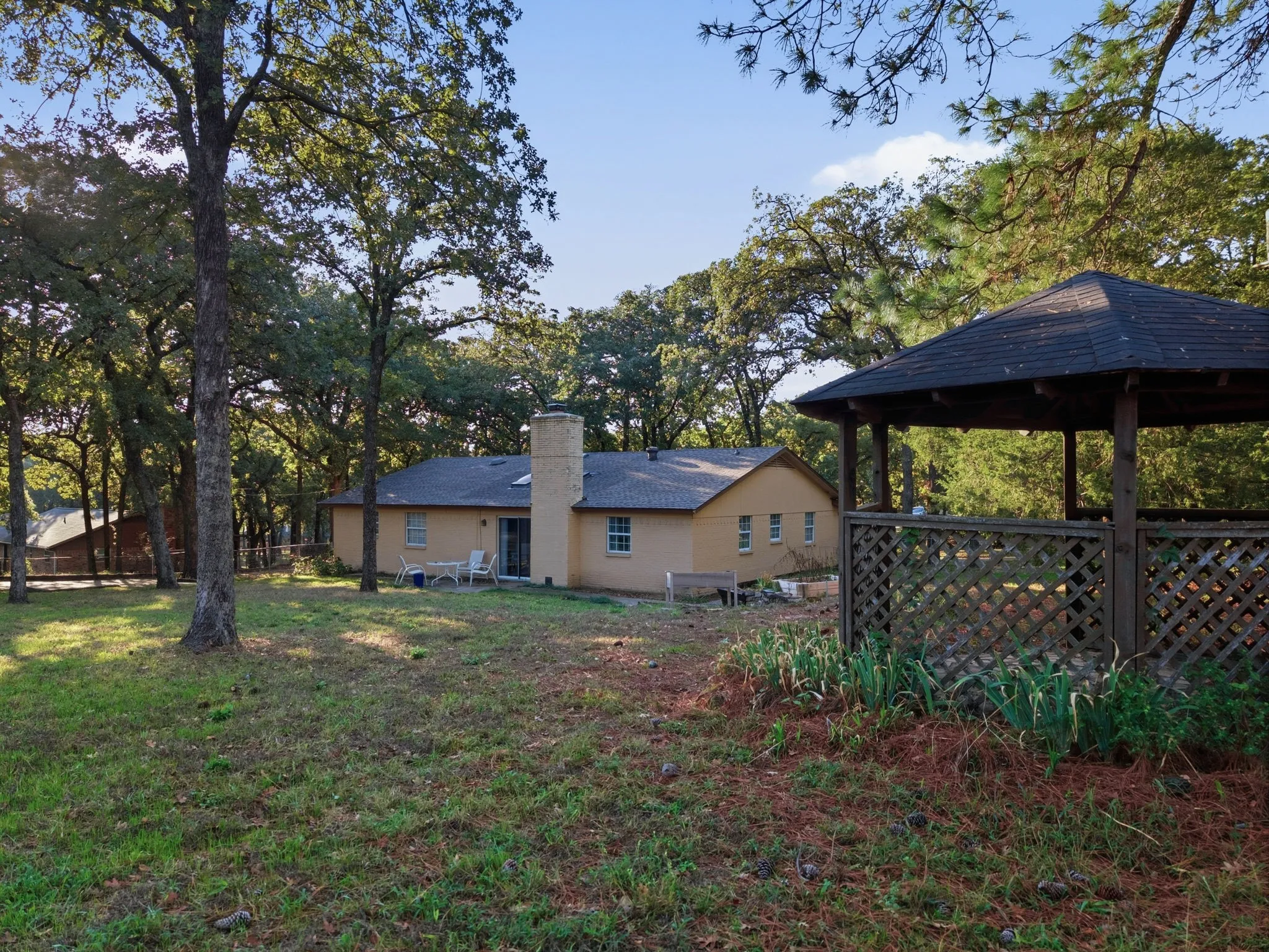 Spacious backyard oasis featuring mature oak trees, a covered gazebo with lattice detailing, a detached storage structure, and lush lawn area ideal for outdoor entertaining and recreation