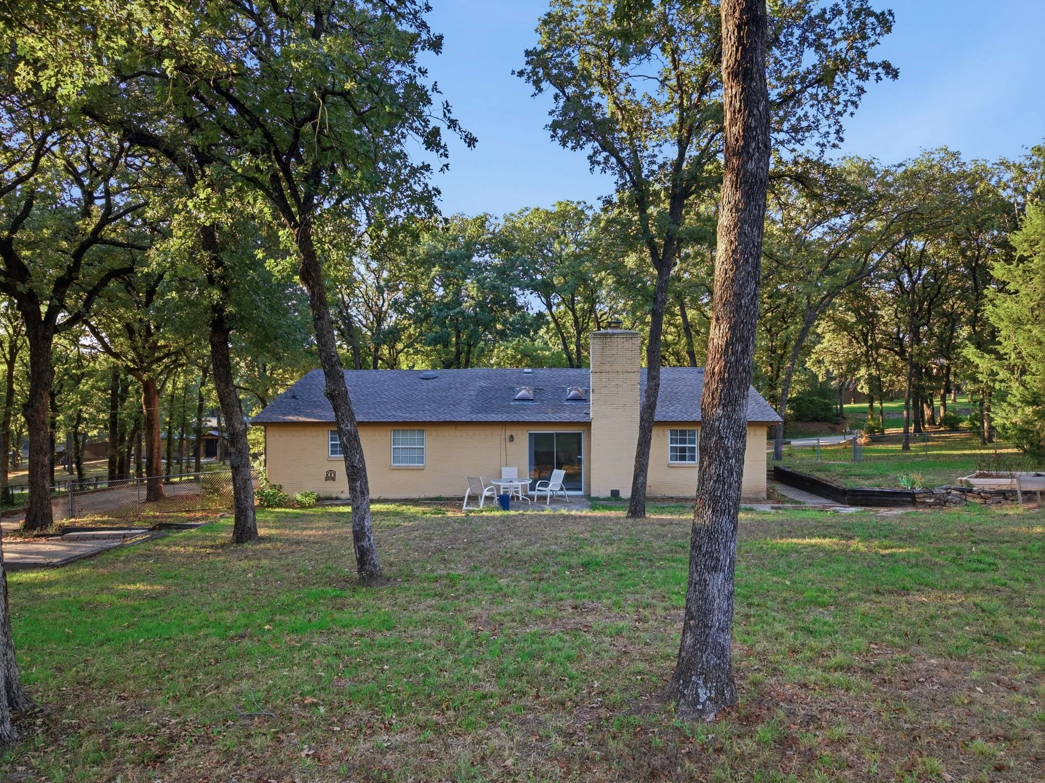 Expansive rear yard with mature trees, a brick exterior, and a built-in chimney