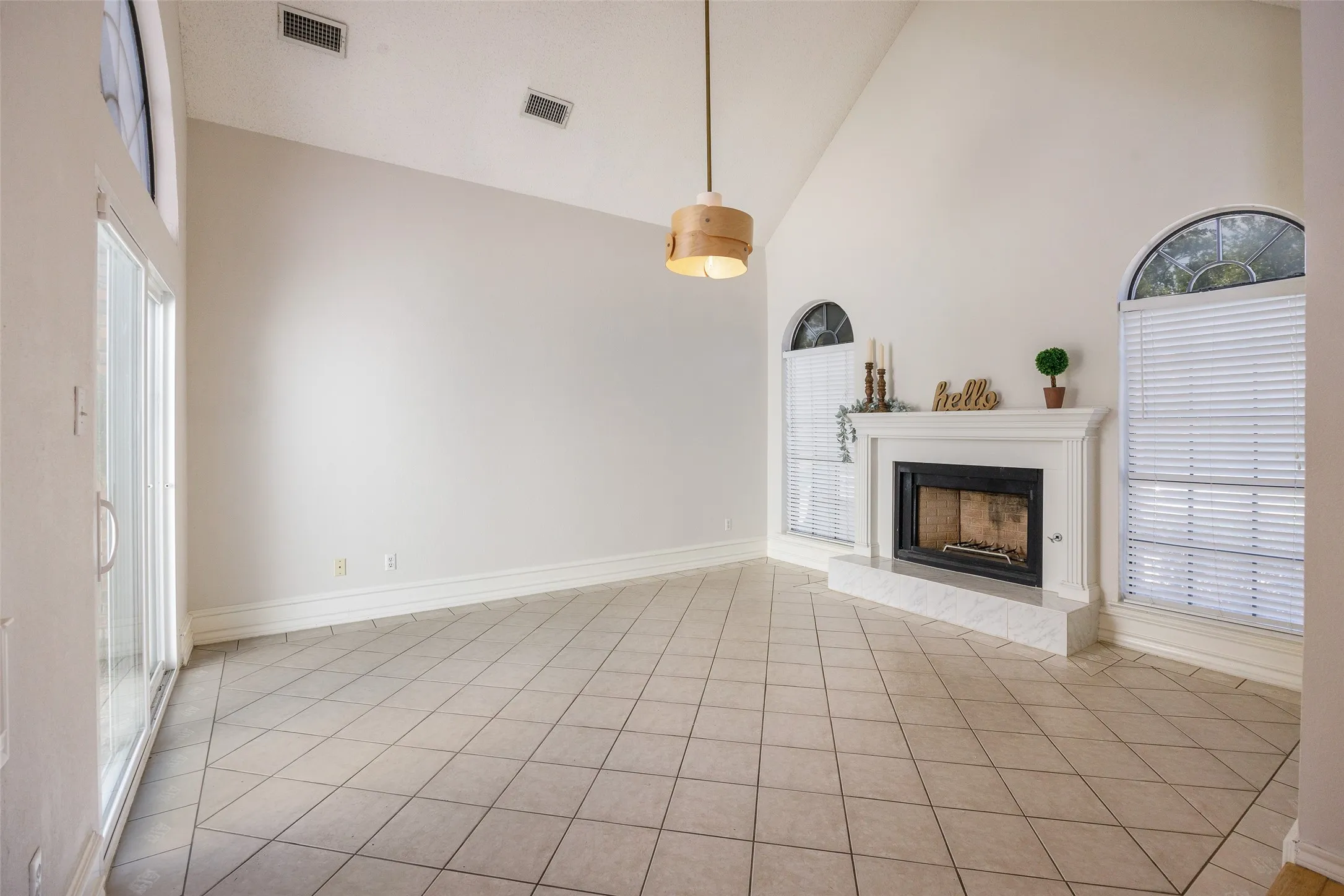 Vaulted ceilings, tile flooring, fireplace with a mantel, arched windows, and a multi-pane glass door