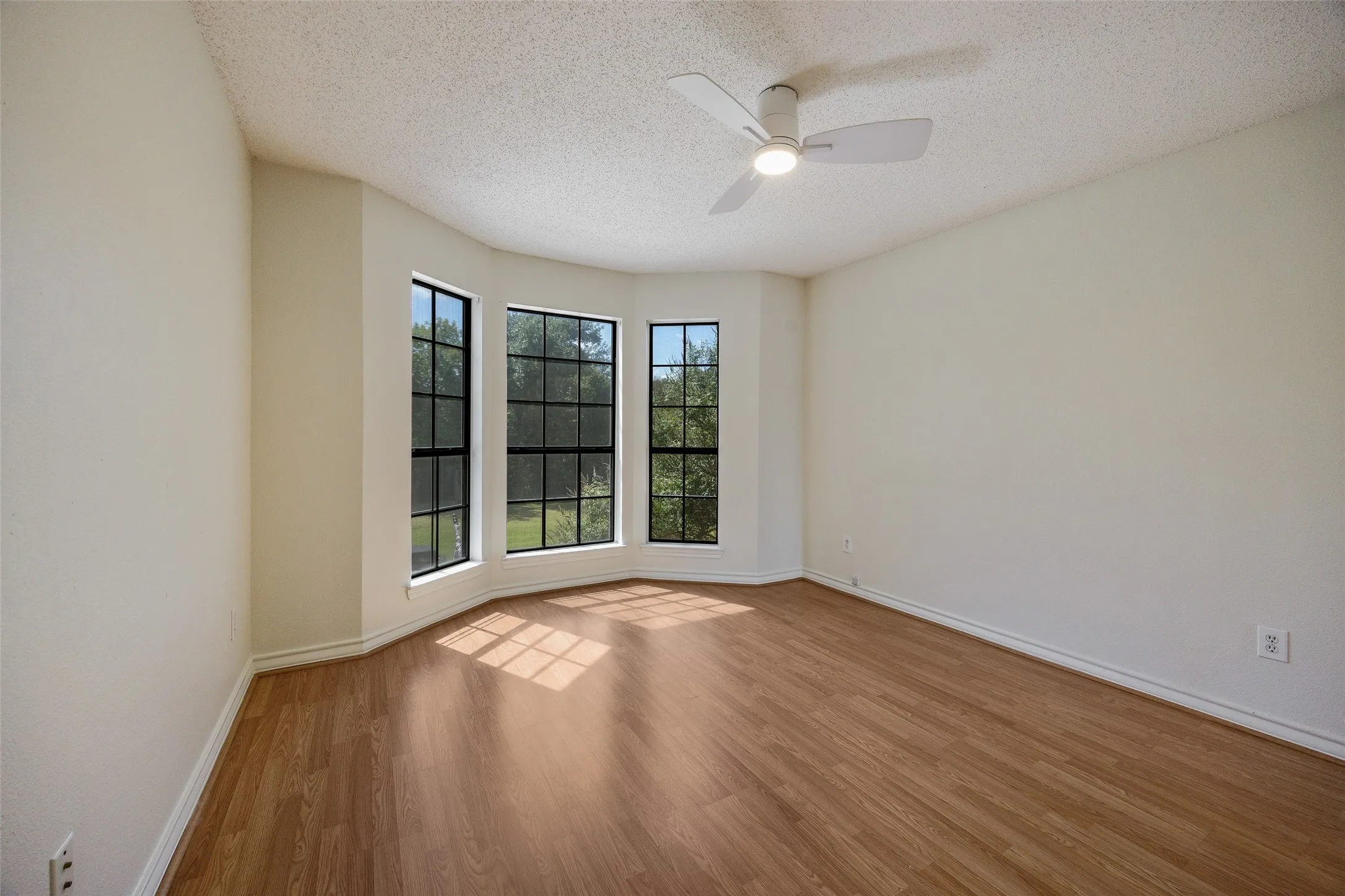 Bay window with multi-pane glazing, wood-finish flooring, and a ceiling-mounted light fixture with fan