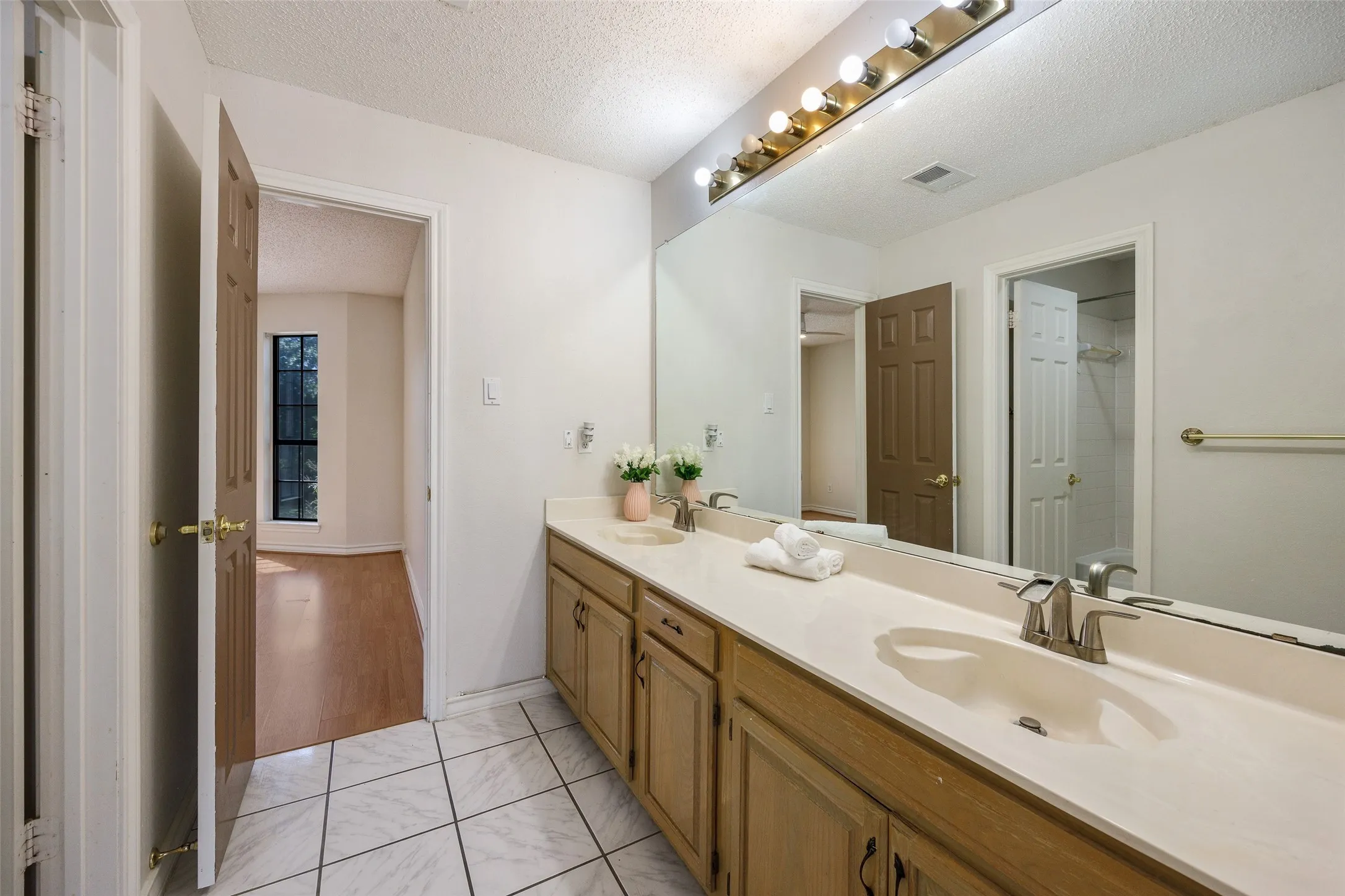 Bathroom featuring a dual-sink vanity, expansive wall-to-wall mirror, multi-bulb light fixture, and tile flooring