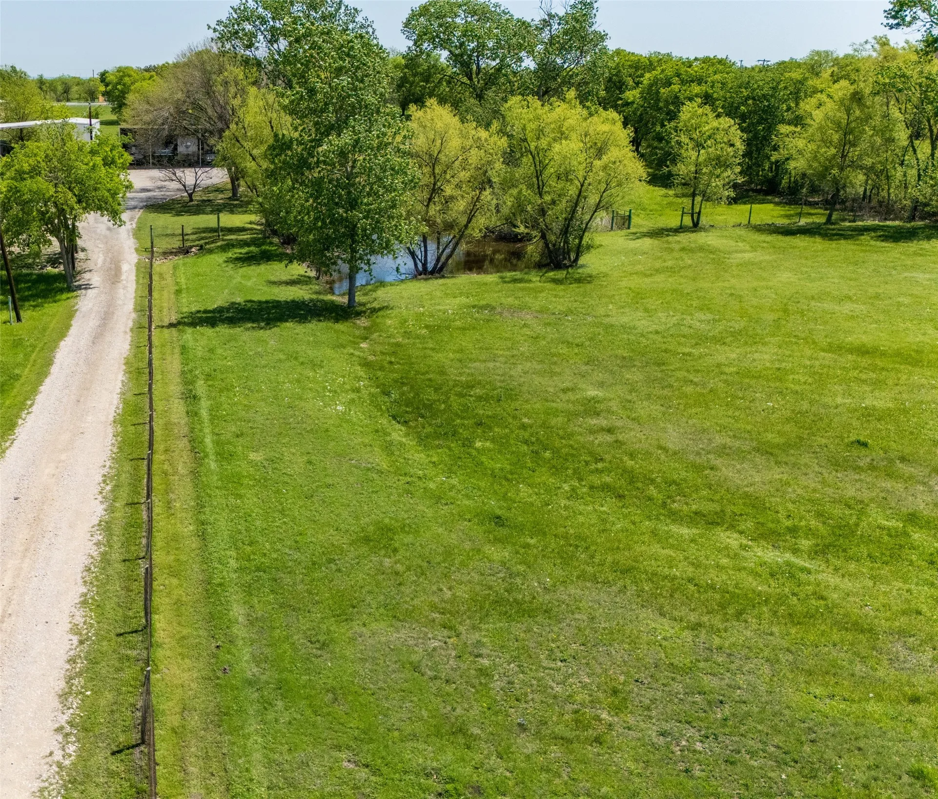 Expansive acreage featuring a gravel driveway, a private pond, perimeter fencing, and mature trees