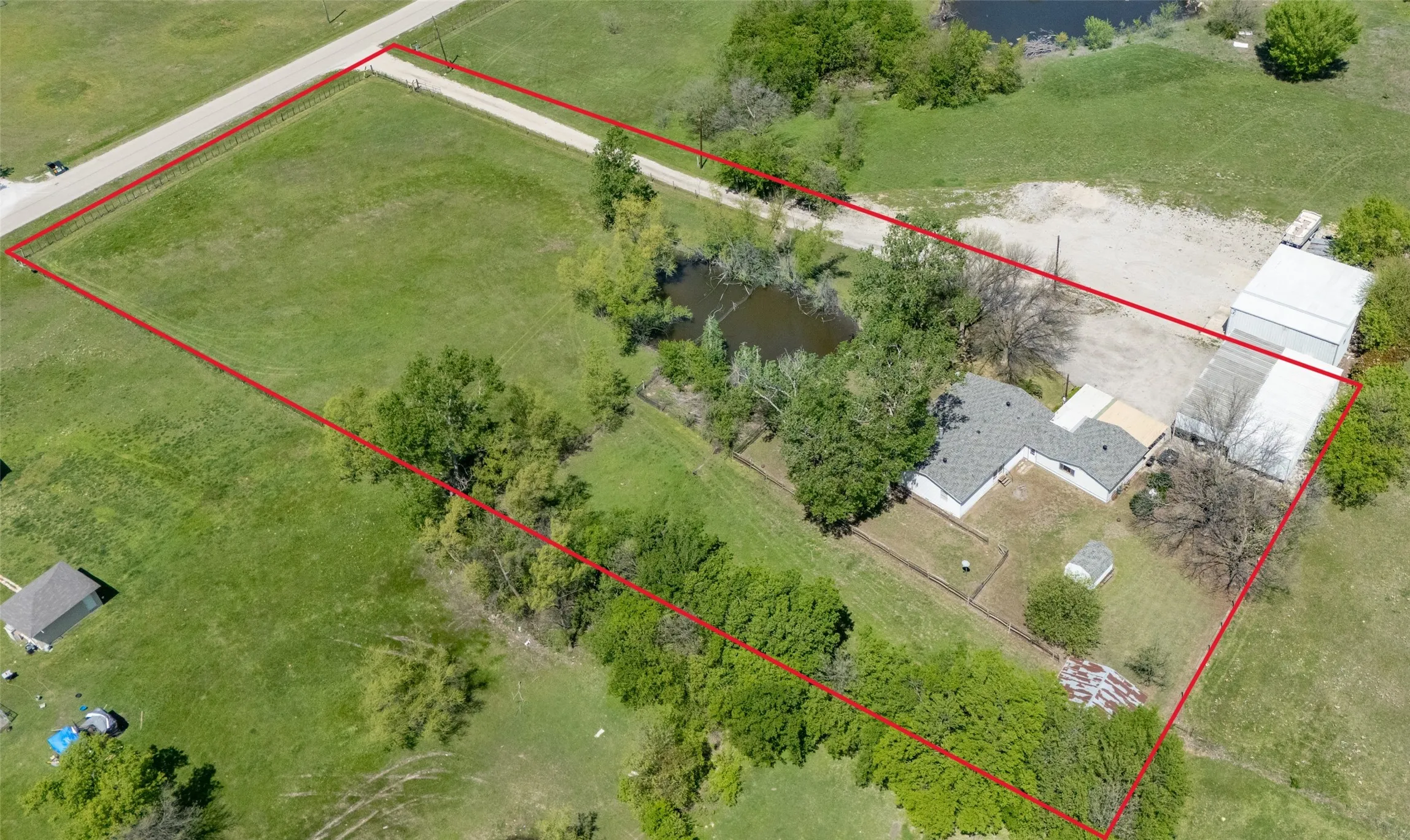 Expansive acreage featuring a private pond, mature tree canopy, multiple detached structures, and extensive open green space