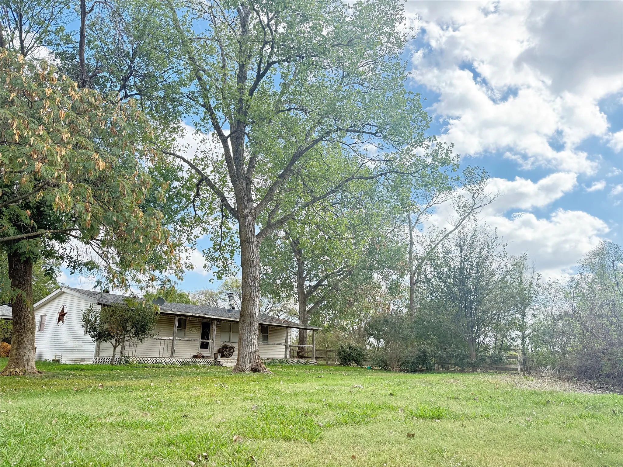 Single-story exterior featuring a covered front porch, light-toned siding, and a sprawling lot with established mature trees