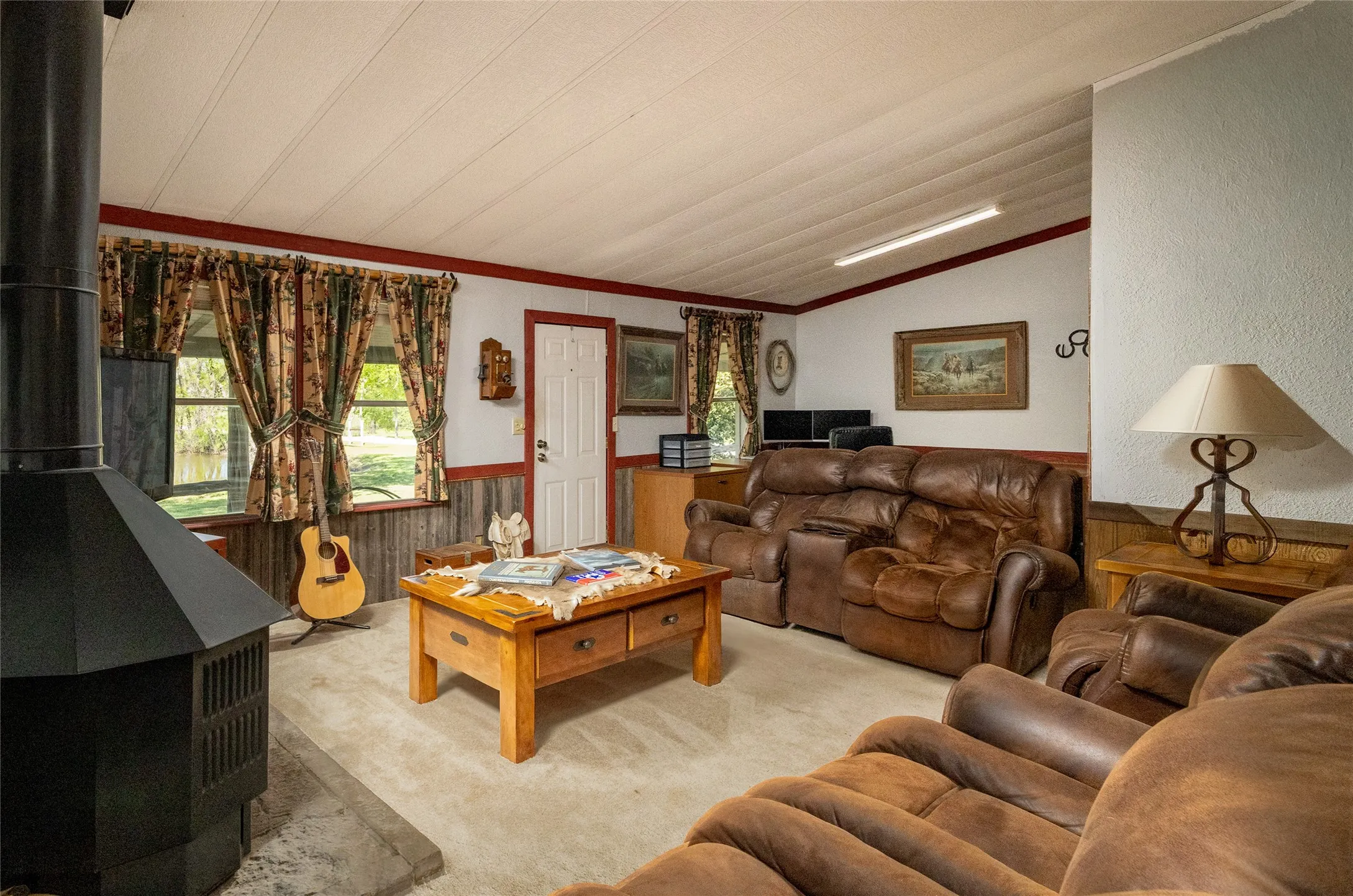 Vaulted ceiling, wood-burning stove with a stone hearth, wainscoting, and multi-pane windows