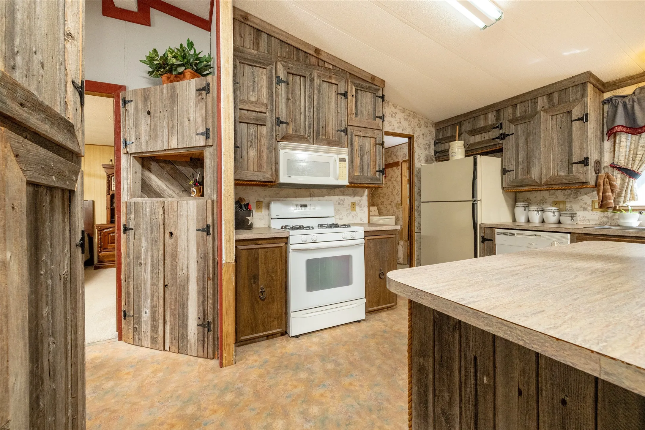 Kitchen featuring custom rustic wood cabinetry with exposed hinge hardware, a central island with a laminate countertop, and a white built-in microwave and gas range
