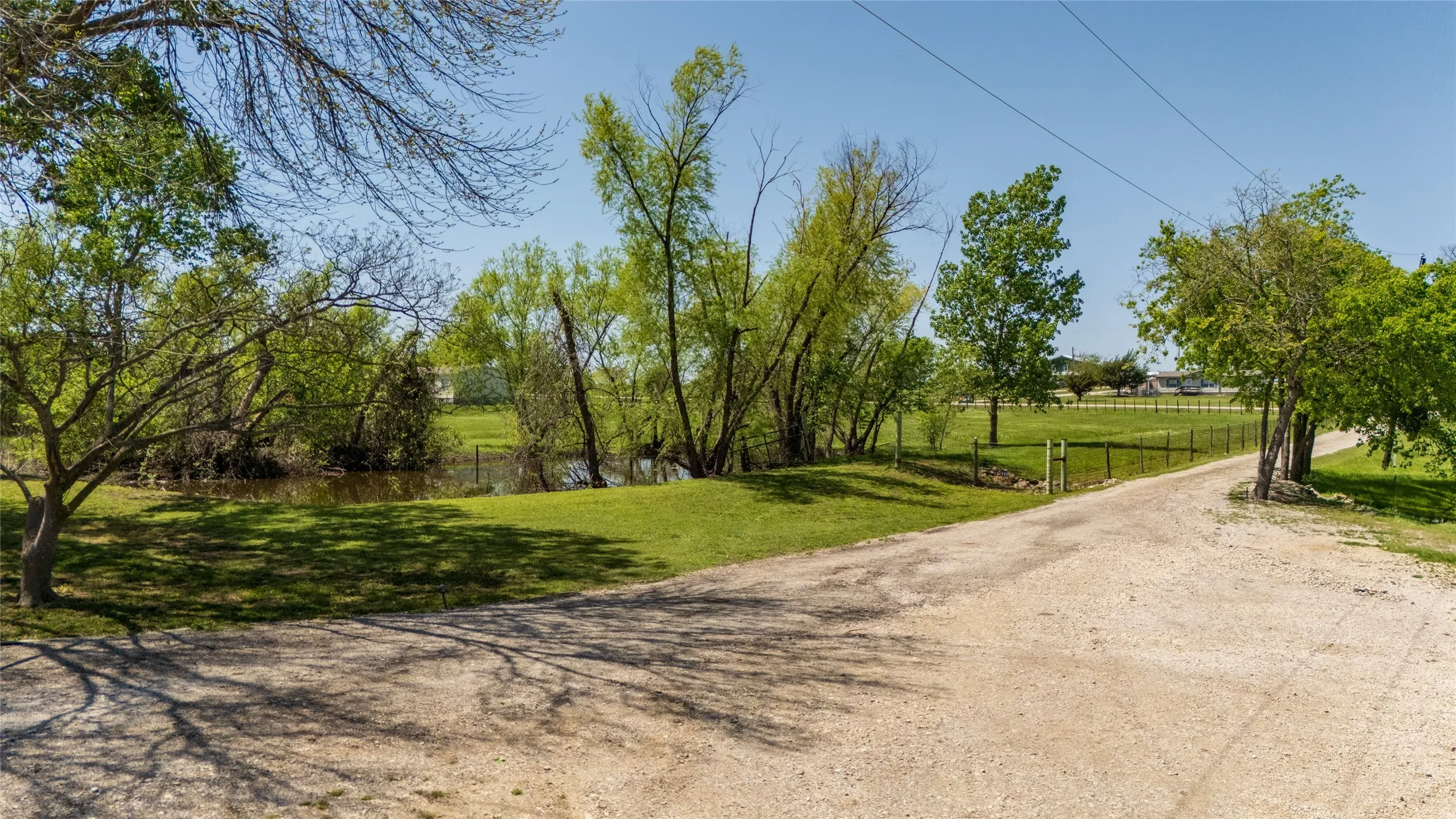 Expansive lot featuring a natural pond, mature trees, open grassy areas, and a gravel driveway