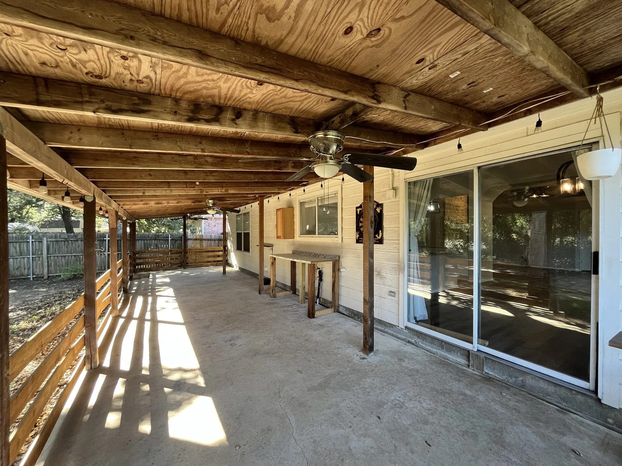 Expansive covered patio featuring a concrete surface, exposed wood beam ceiling, multiple ceiling fans, and string lighting